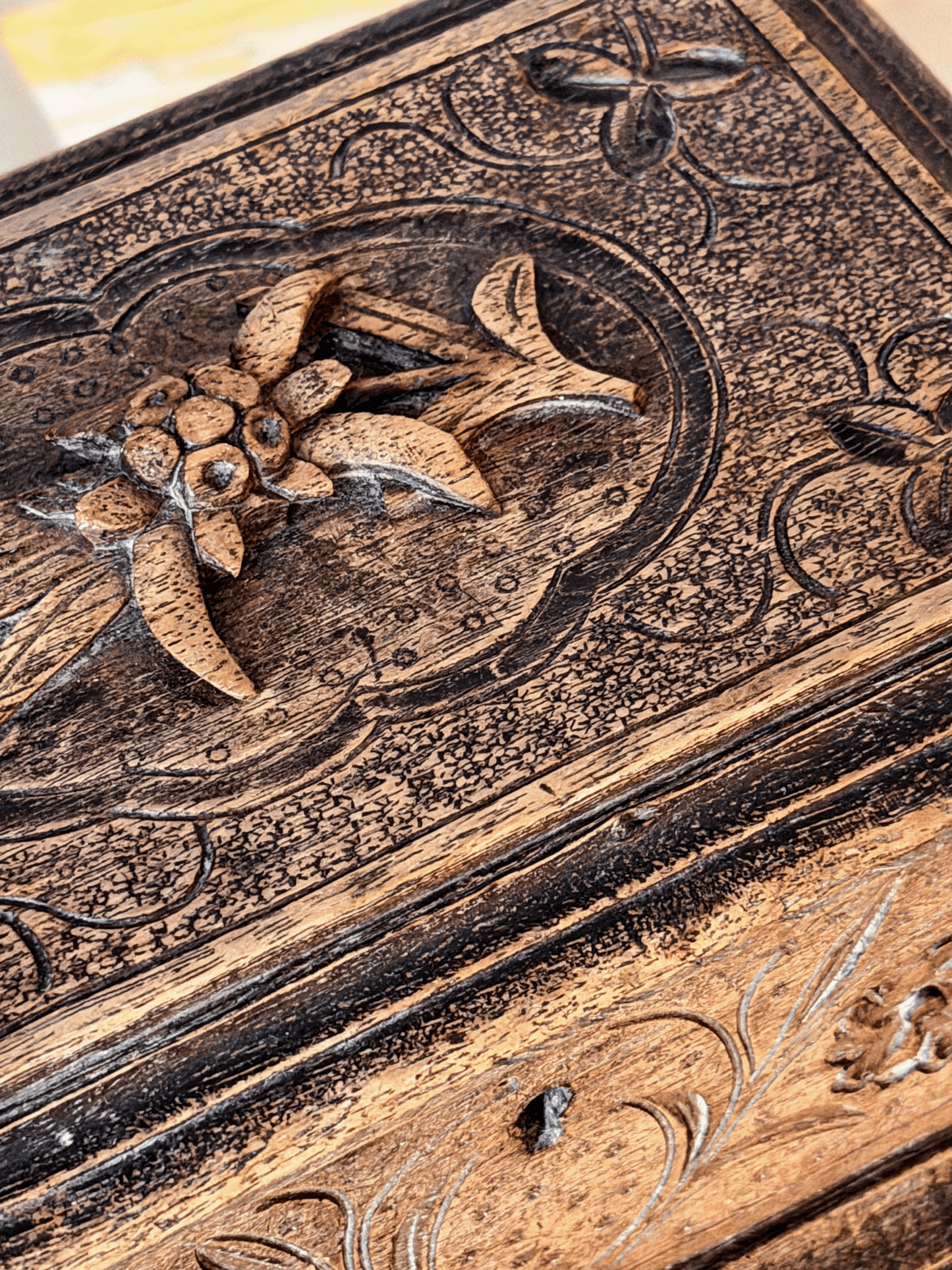 Close-up of a carved wooden box lid featuring floral and scroll motifs in dark brown and natural tan wood tones.