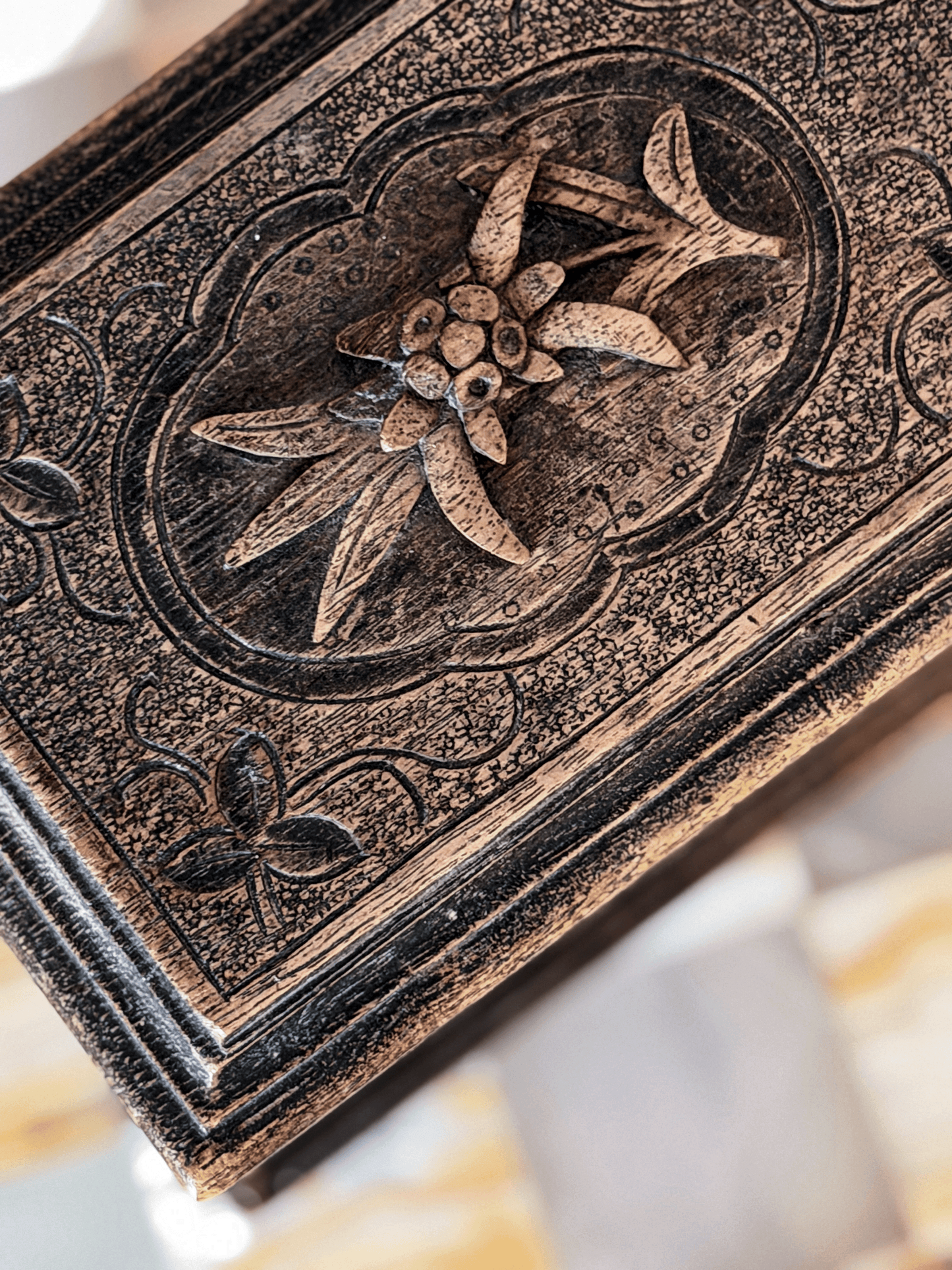 Close-up of the lid of an antique Brienz Black Forest style Swiss wood box, showcasing a high-relief hand-carved edelweiss mountain flower inside a scalloped frame against a hand-stippled background.
