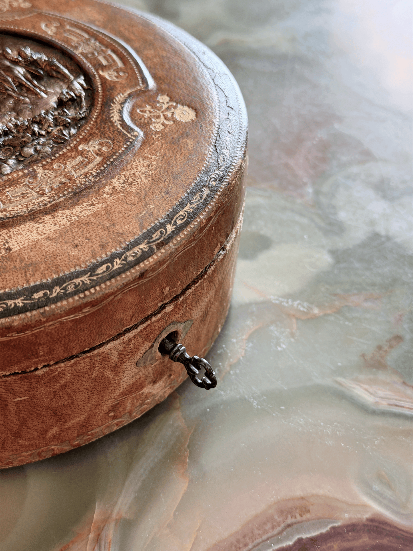 Antique French Grand Tour leather vanity box from the early 20th century, showing a green tooled Morocco leather exterior with a central cast bronze repoussé plaque depicting a classical pastoral garden party scene, with original steel barrel key.