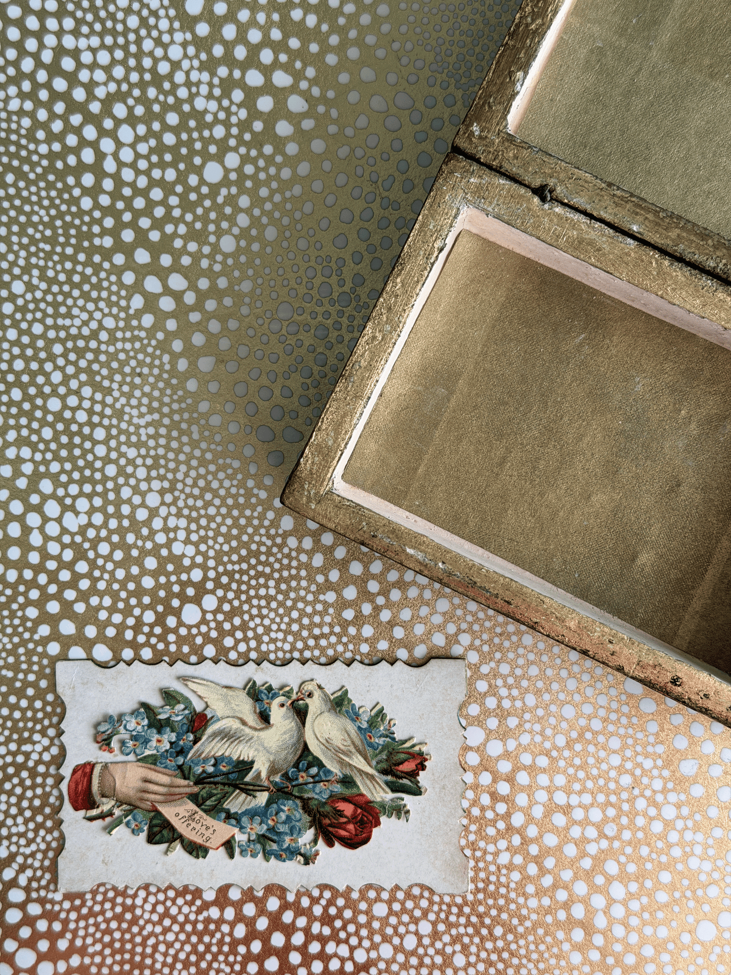 An open vintage-style wooden box with a gold-toned interior, placed on a patterned surface alongside a small illustrated card featuring two white doves and red roses.
