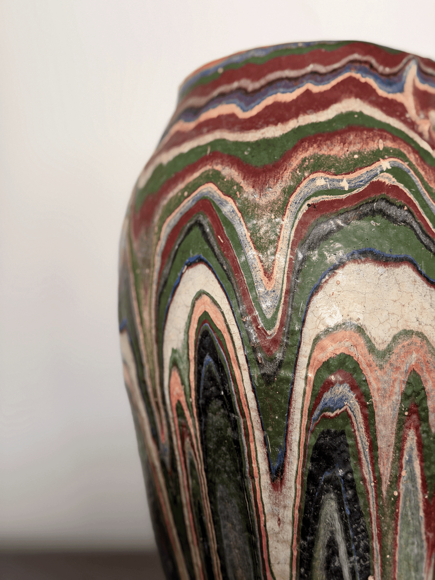 Close-up of ozark pottery vase with a marbled, wavy pattern in green, red, cream, black, and blue drip glaze.