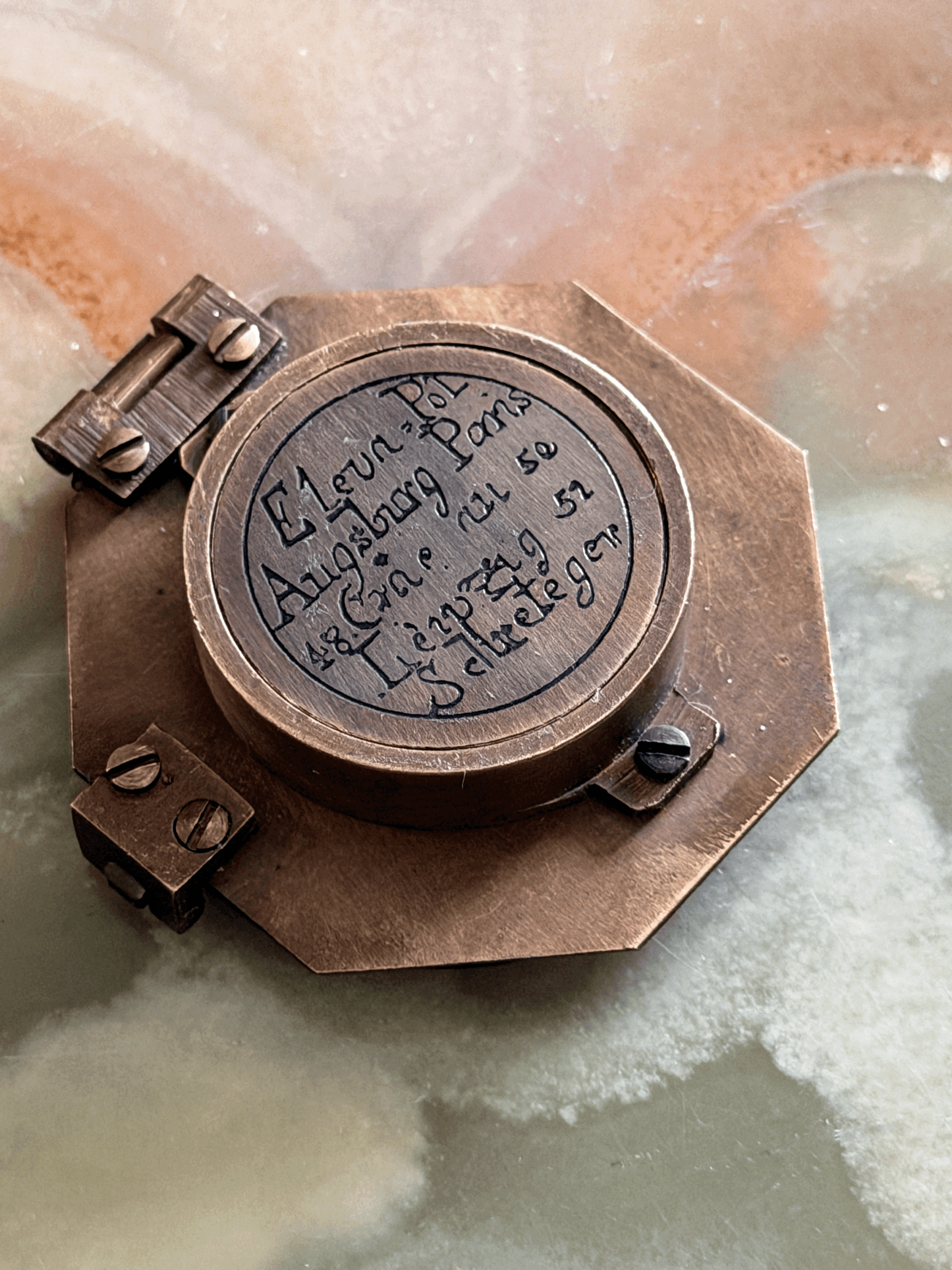 Engraved underside of a reproduction brass pocket sundial, replicating an 18th-century German instrument with an Elev. Pol. latitude table for Augsburg, Paris, Cracau, and Liège alongside the maker signature Schretegger.