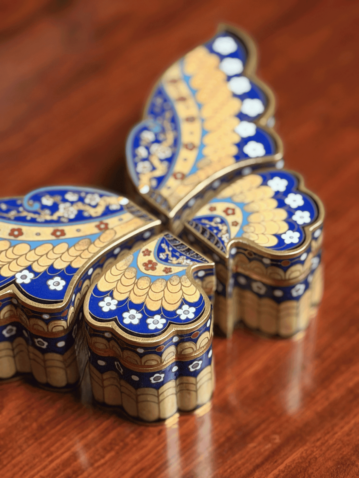 Decorative butterfly-shaped box with blue and gold patterns on a wooden surface