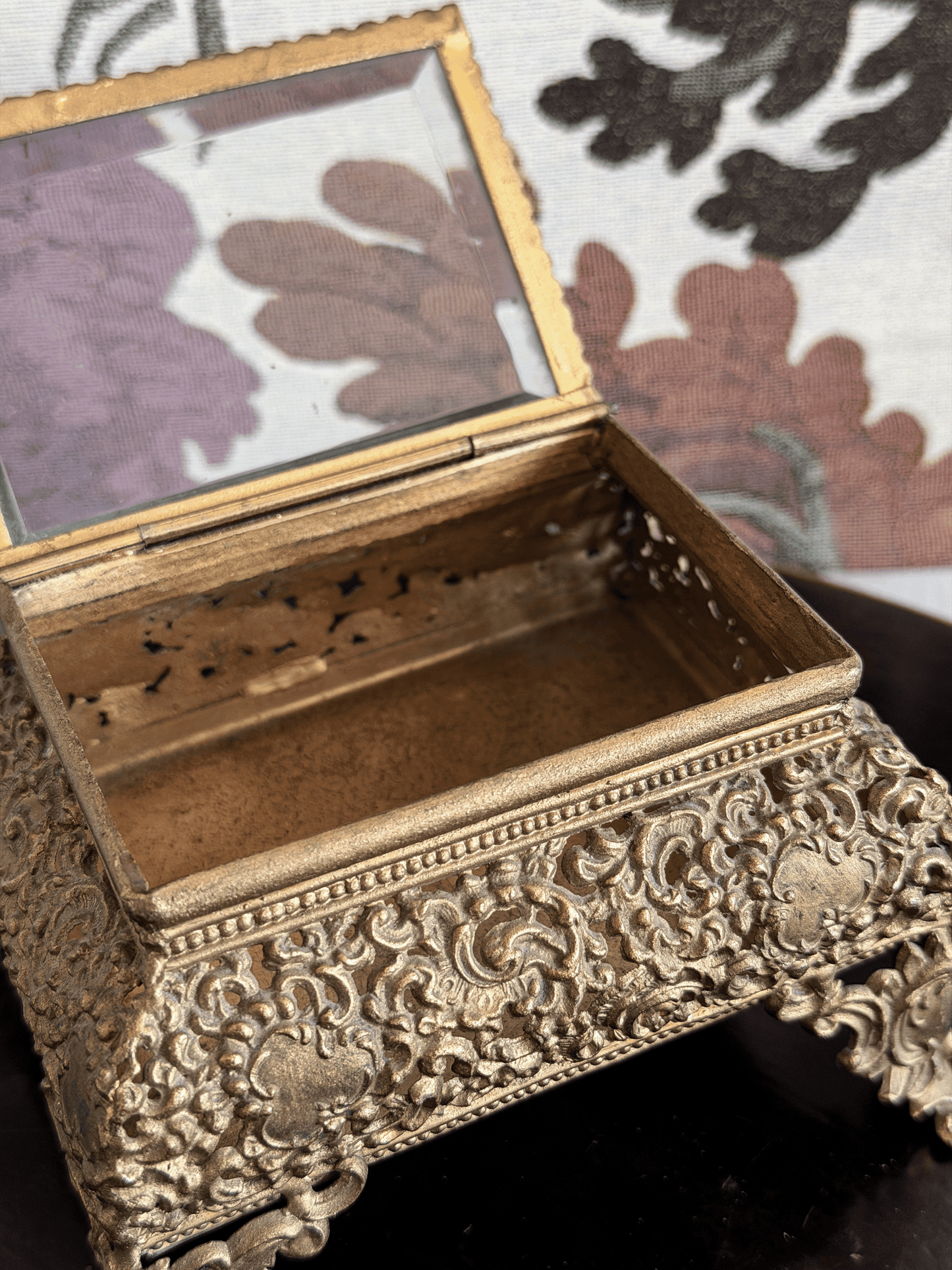 Open vintage gold filigree jewelry box casket with raised ornate scroll feet and an attached hinged glass lid.