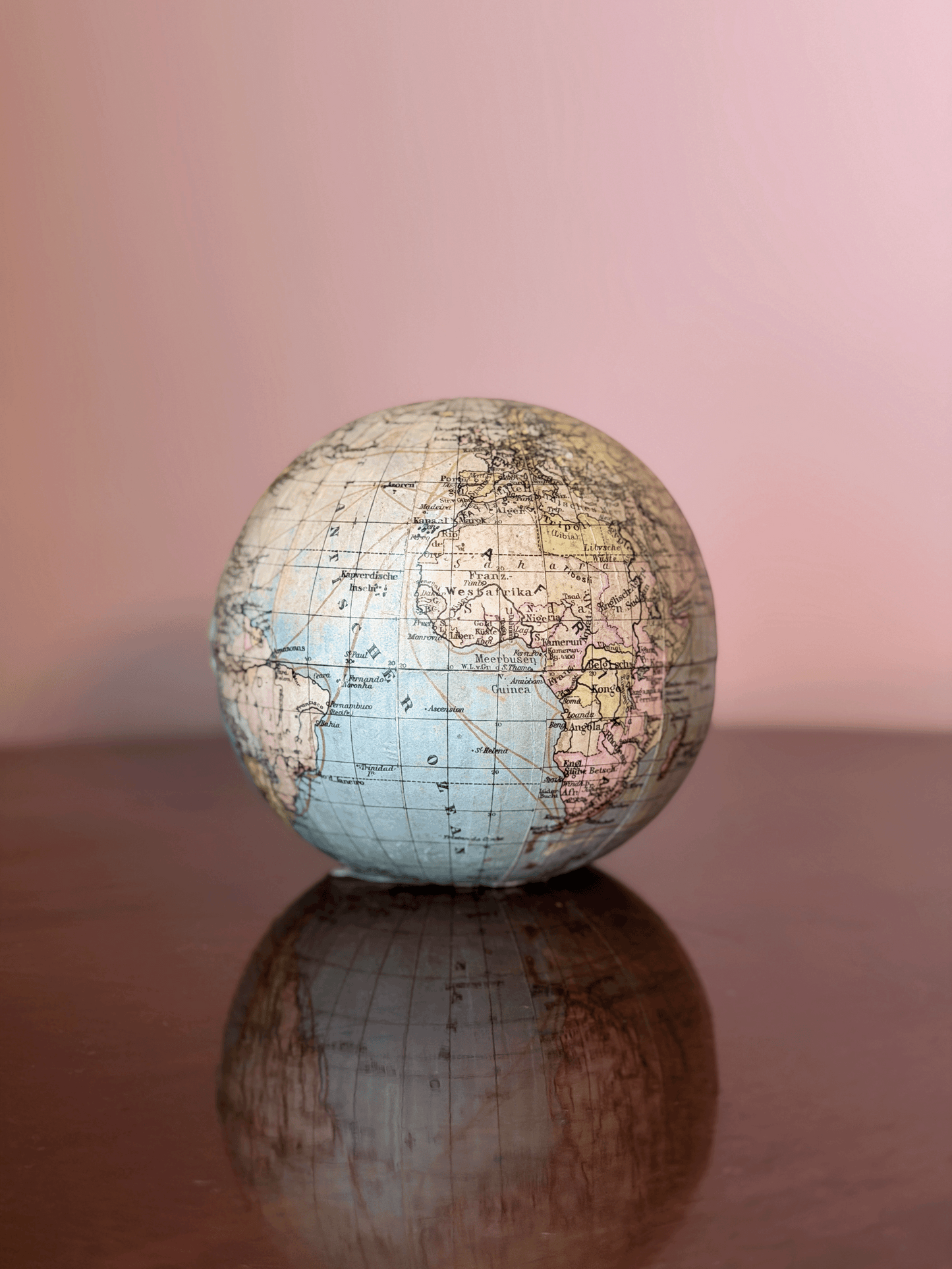 Rare 1920s antique German paper-mâché world globe bank by Paul Räth Leipzig, hand-wrapped in paper map gores showing an amber sepia patina, craquelure varnish, and a narrow coin slot cut directly into the North Pole.