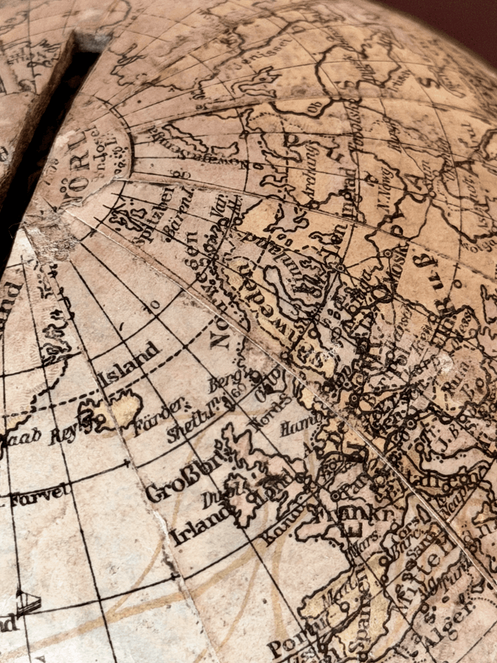 Rare 1920s antique German paper-mâché world globe bank by Paul Räth Leipzig, hand-wrapped in paper map gores showing an amber sepia patina, craquelure varnish, and a narrow coin slot cut directly into the North Pole.