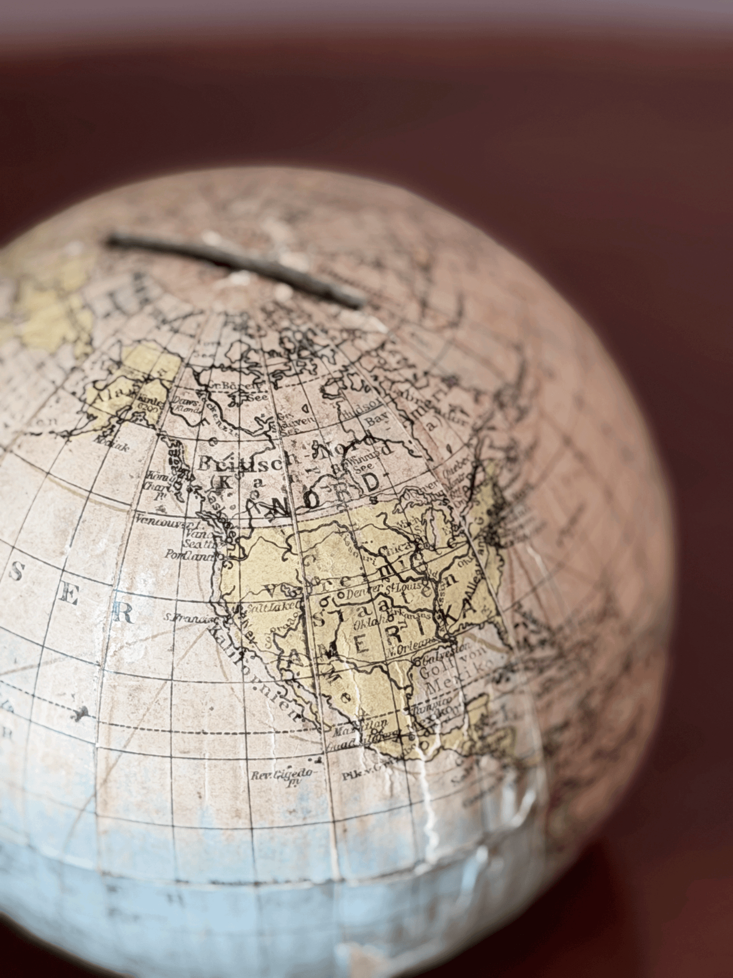 Rare 1920s antique German paper-mâché world globe bank by Paul Räth Leipzig, hand-wrapped in paper map gores showing an amber sepia patina, craquelure varnish, and a narrow coin slot cut directly into the North Pole.
