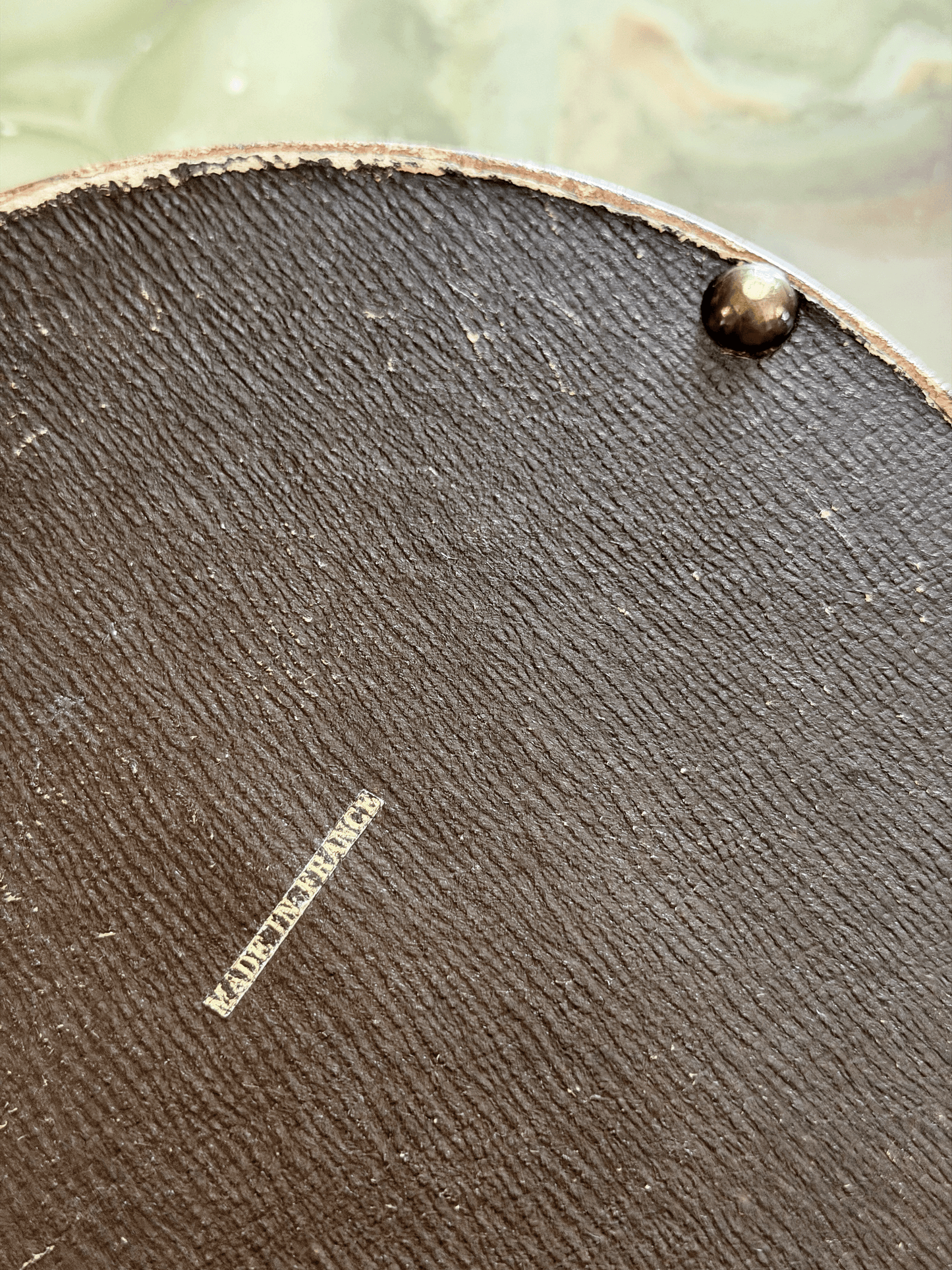 Close-up of the leather-wrapped underside of an antique French vanity box, showing a crisp block-font export stamp reading MADE IN FRANCE applied in metallic gold foil.