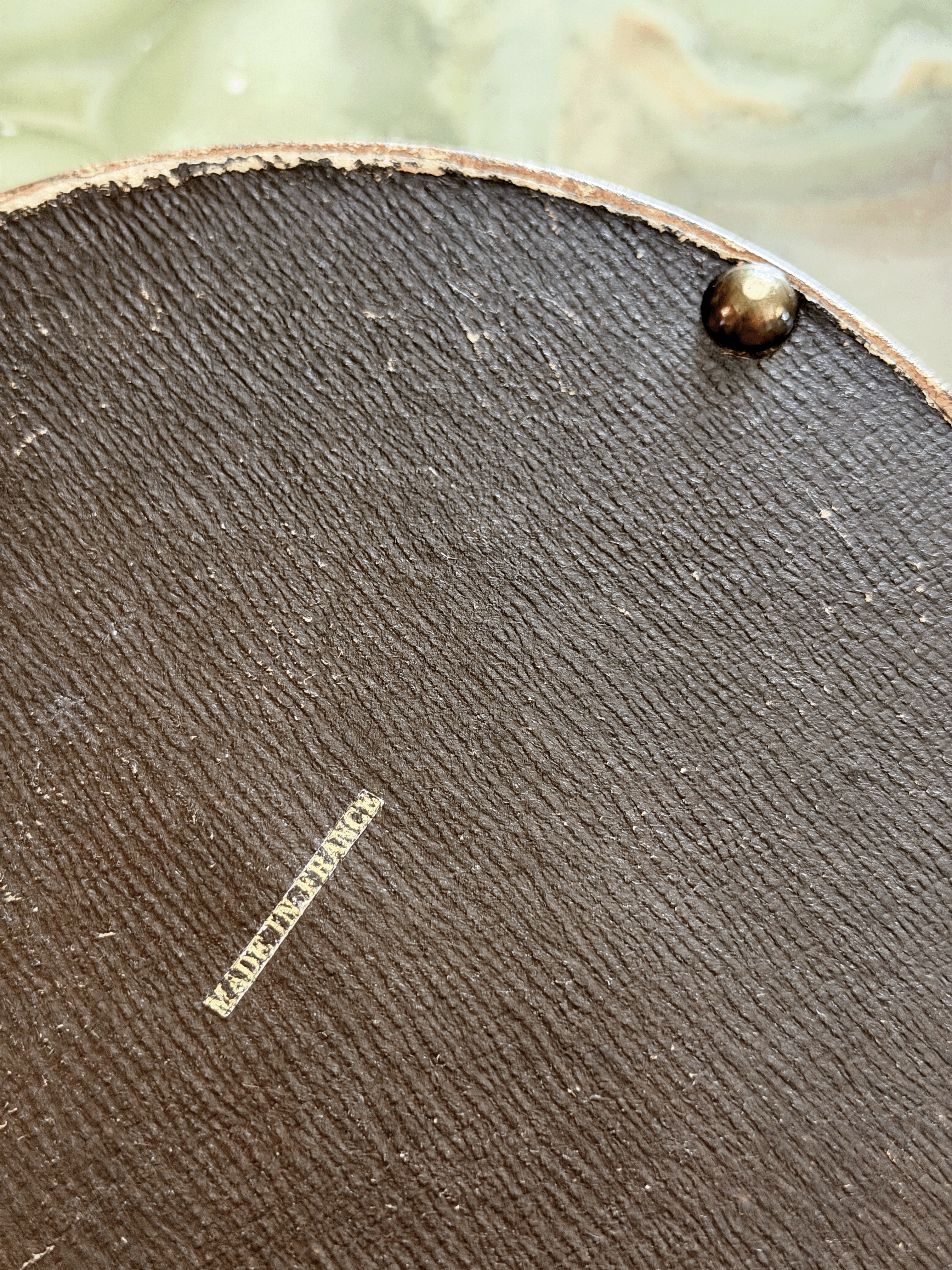 Close-up of the leather-wrapped underside of an antique French vanity box, showing a crisp block-font export stamp reading MADE IN FRANCE applied in metallic gold foil.