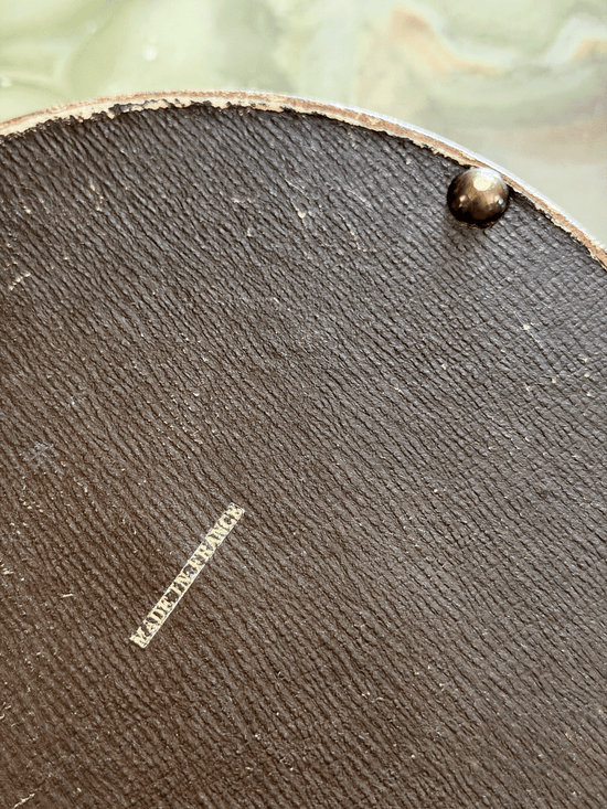 Close-up of the leather-wrapped underside of an antique French vanity box, showing a crisp block-font export stamp reading MADE IN FRANCE applied in metallic gold foil.