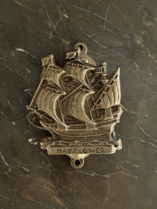 Vintage mid-century solid brass door knocker cast in the shape of the historical Mayflower pilgrim sailing ship, featuring a detailed multi-masted galleon hull with a dark aged patina in the recessed engraving.