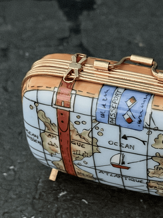 Close-up of a Rochard porcelain map suitcase trinket box, emphasizing hand-painted ocean geography reading Ocean Atlantique and Amerique alongside an illustrated historic red-sailed galleon ship.