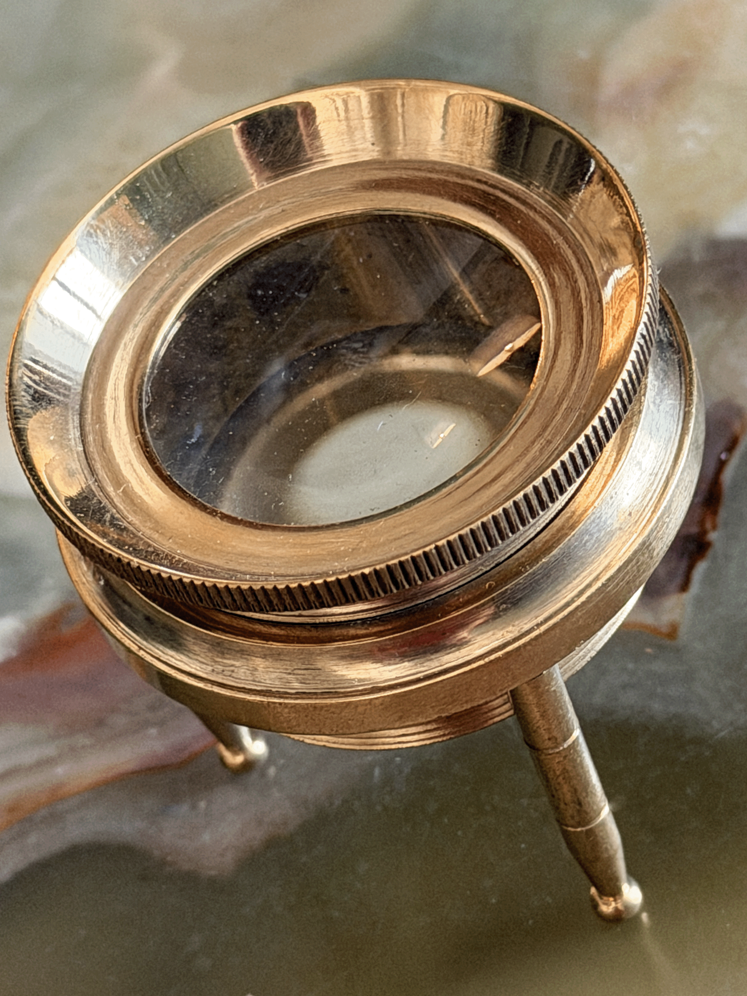 A close-up of a brass magnifying glass tripod stand with a polished brass finish and a clear glass lens