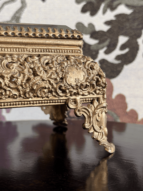Close-up of an ornate gold-toned decorative jewelry box with intricate carved scrollwork and cabriole-style legs.