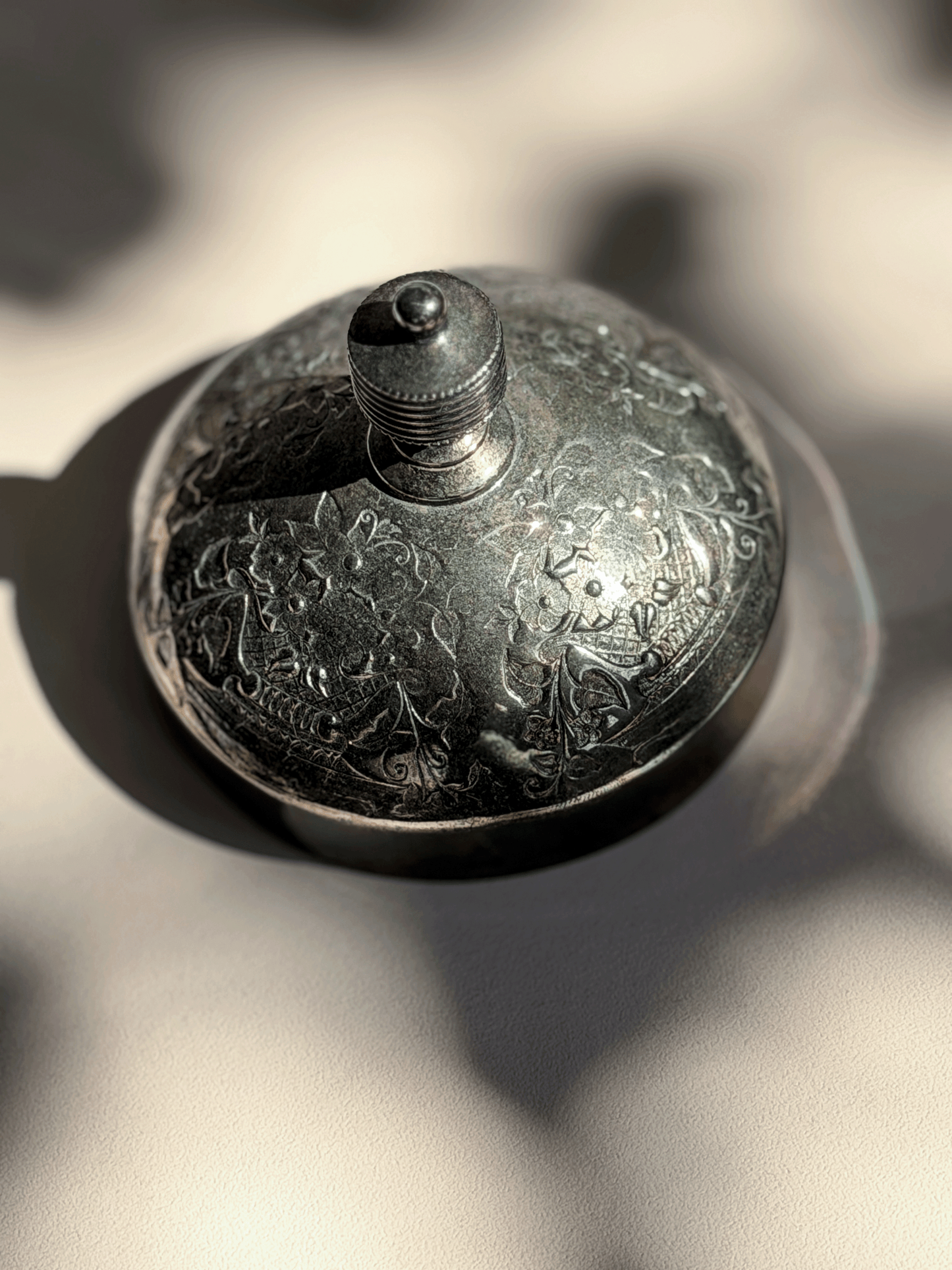 Close-up of an antique silver-plated dome lid with intricate floral repoussé engravings for glass castor jar.