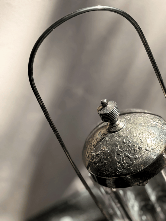 Antique Victorian silver-plated pickle castor featuring a clear vertical-paneled glass jar nested inside a tall, arched lantern-style metal frame with a shadow backdrop.
