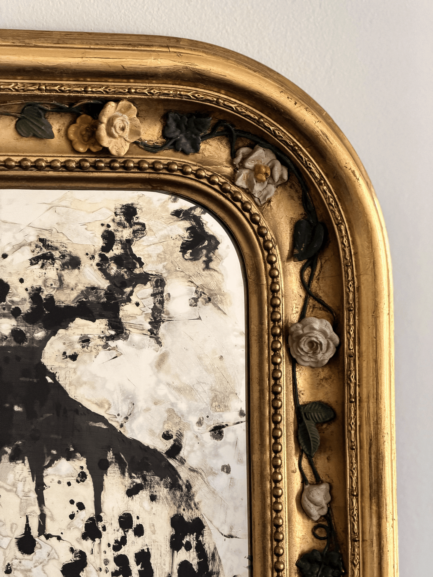 Detailed close-up of a 19th-century French mirror frame showcasing hand-modeled porcelain roses attached to hand-wrought dark metal vine moldings against a brilliant gold leaf gilded finish, next to a heavily foxed antiqued glass mirror plate.