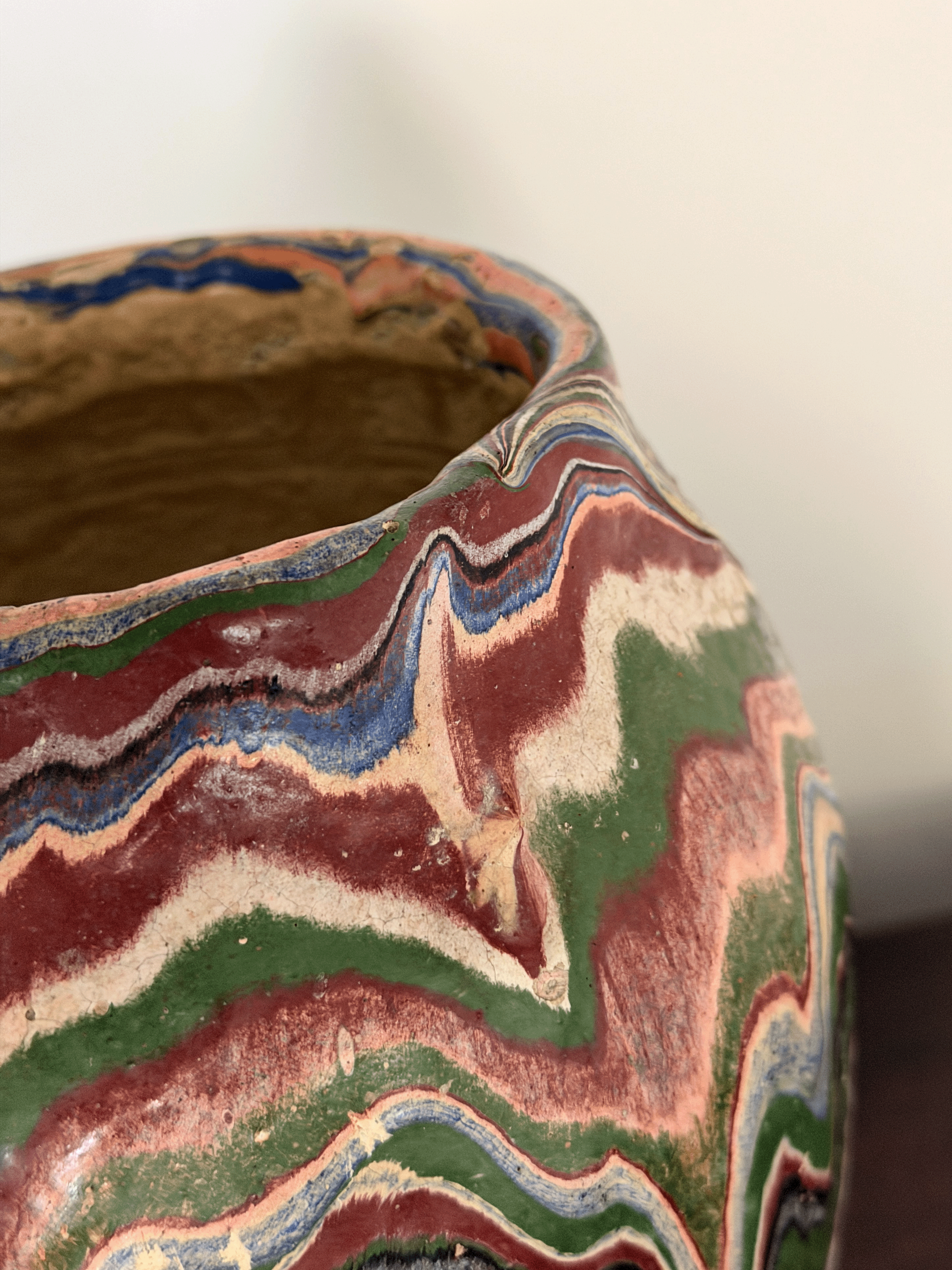 Close-up of a handmade ceramic vase with a marbled, wavy pattern of terracotta red, forest green, cream, and blue glazes.