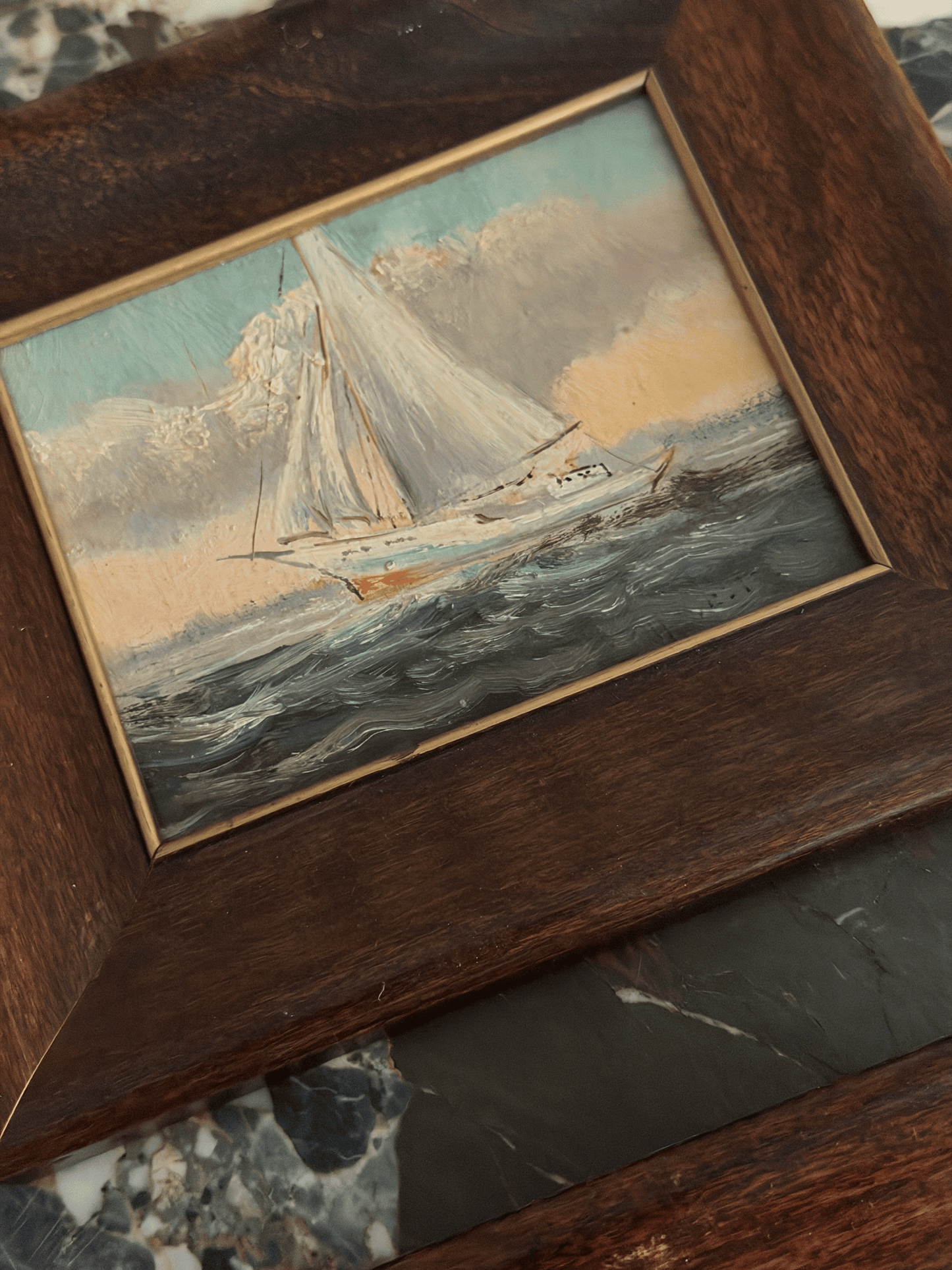 A framed oil painting of a sailboat on the sea, set in a dark brown wooden frame with a gold inner border