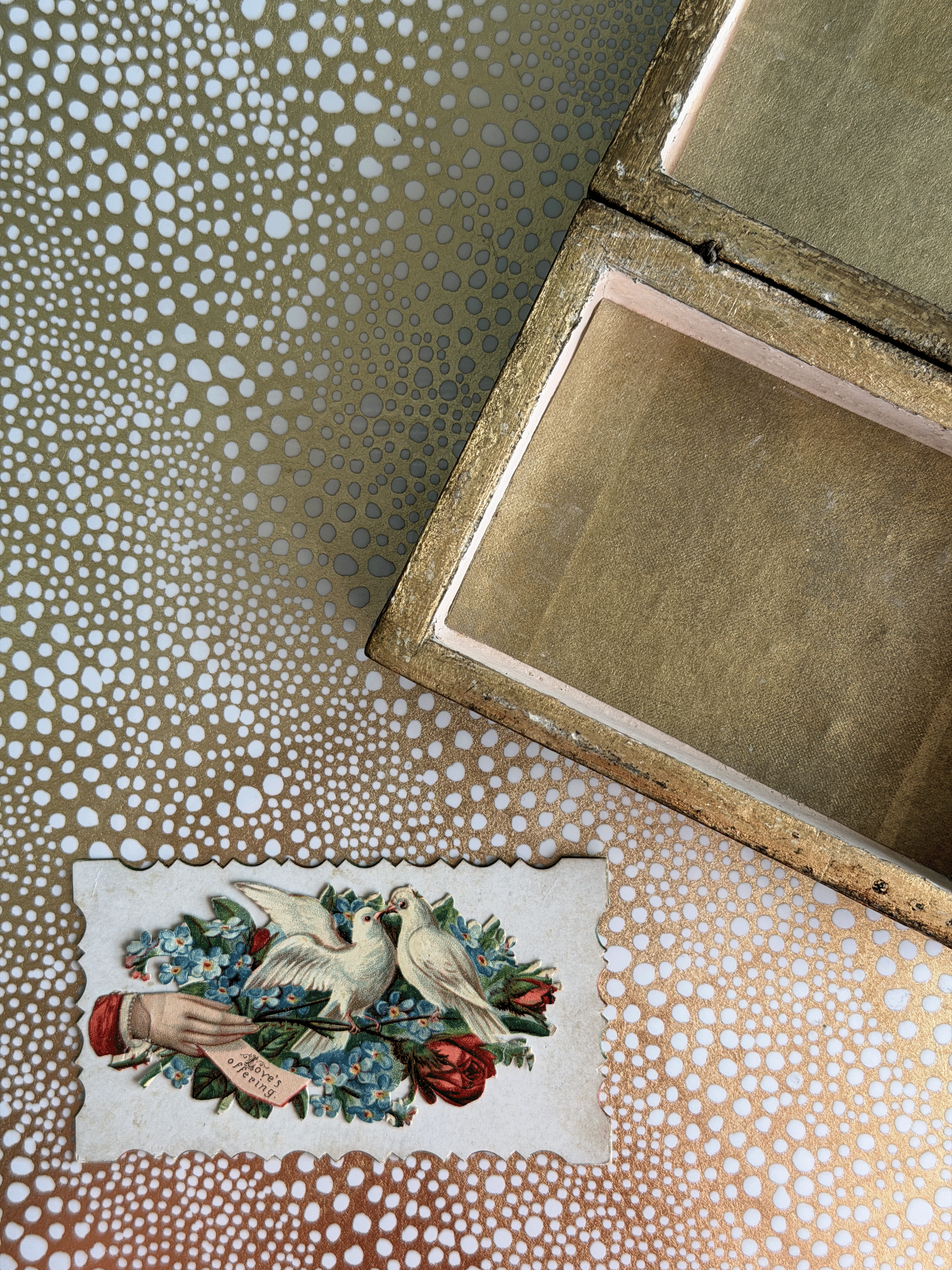 An open vintage-style wooden box with a gold-toned interior, placed on a patterned surface alongside a small illustrated card featuring two white doves and red roses.