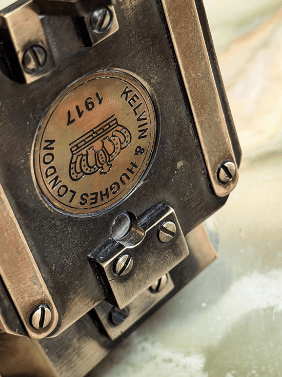 antiqued reproduction brass pocket transit, featuring an inlaid circular brass medallion stamped with a British crown emblem and the historical fantasy hallmark Kelvin and Hughes London 1917.