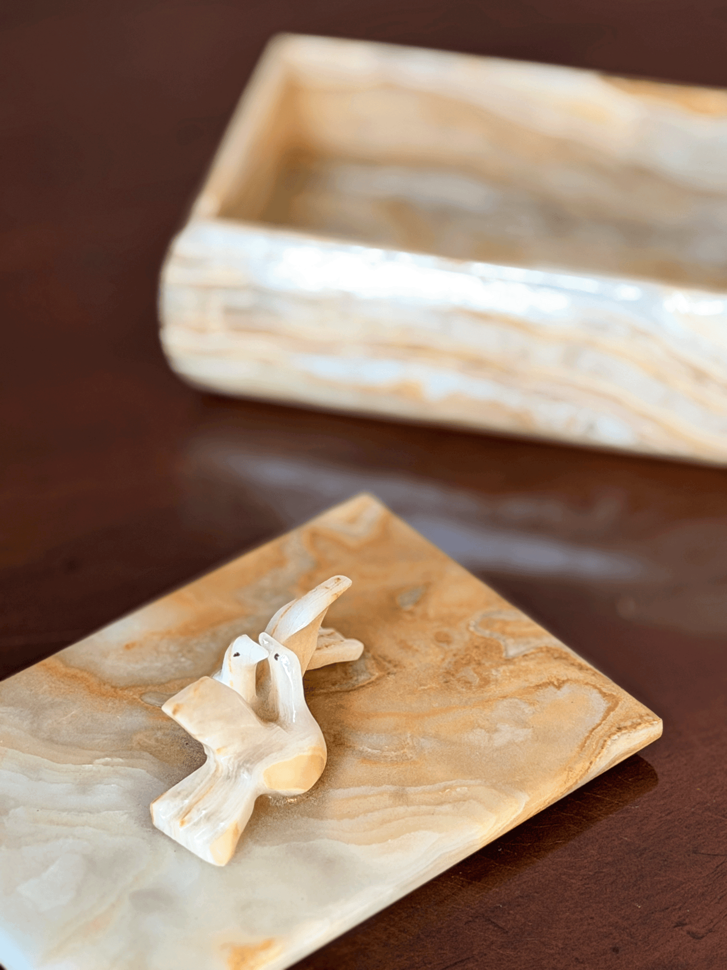 A small carved dove displayed on an onyx, with base tray blurred in the background on a dark brown surface.