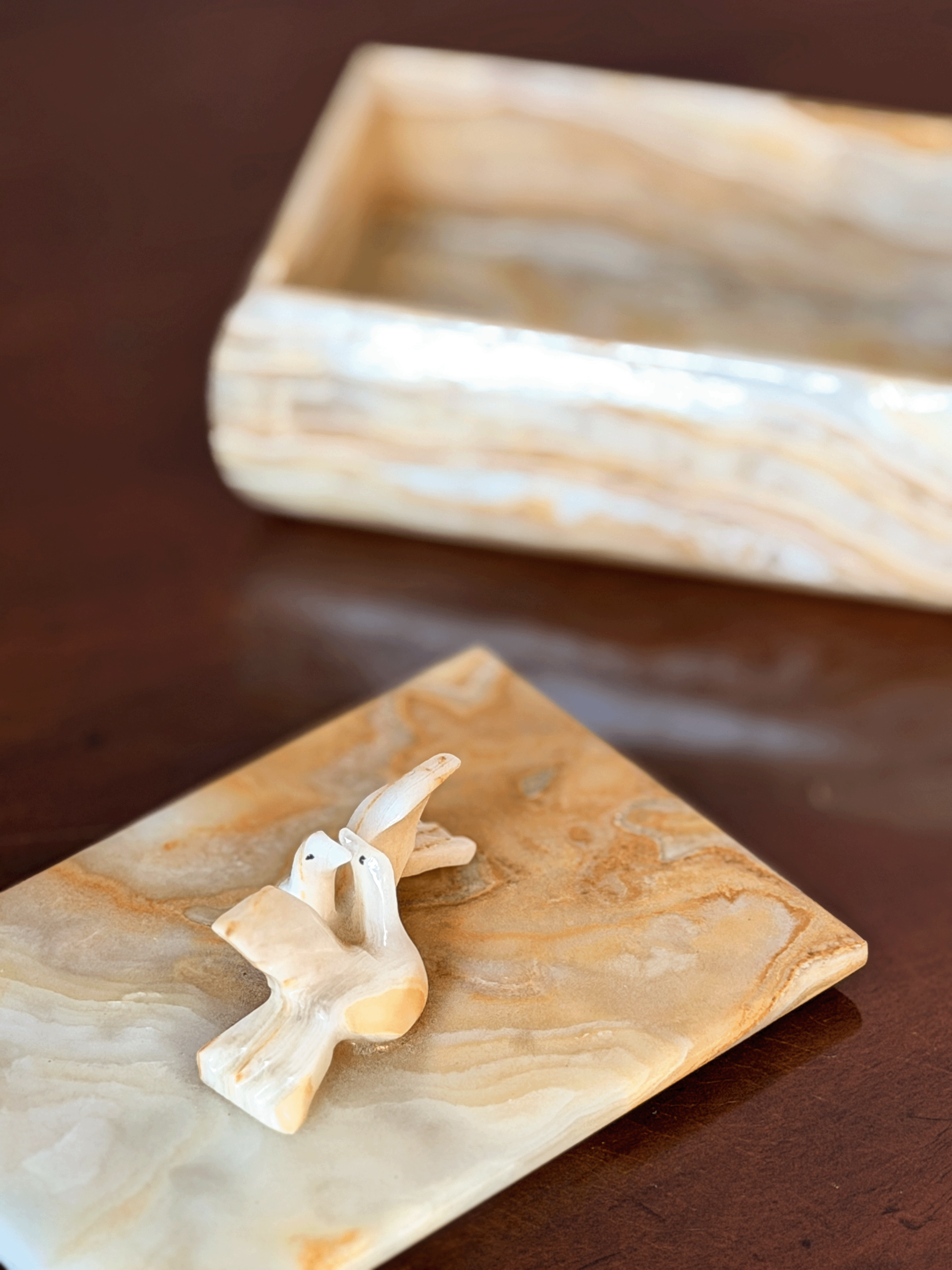 A small carved dove displayed on an onyx, with base tray blurred in the background on a dark brown surface.