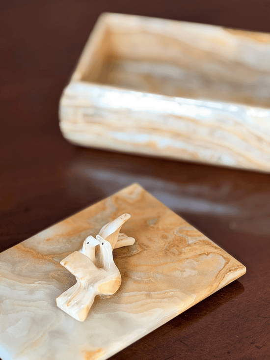 A small carved dove displayed on an onyx, with base tray blurred in the background on a dark brown surface.