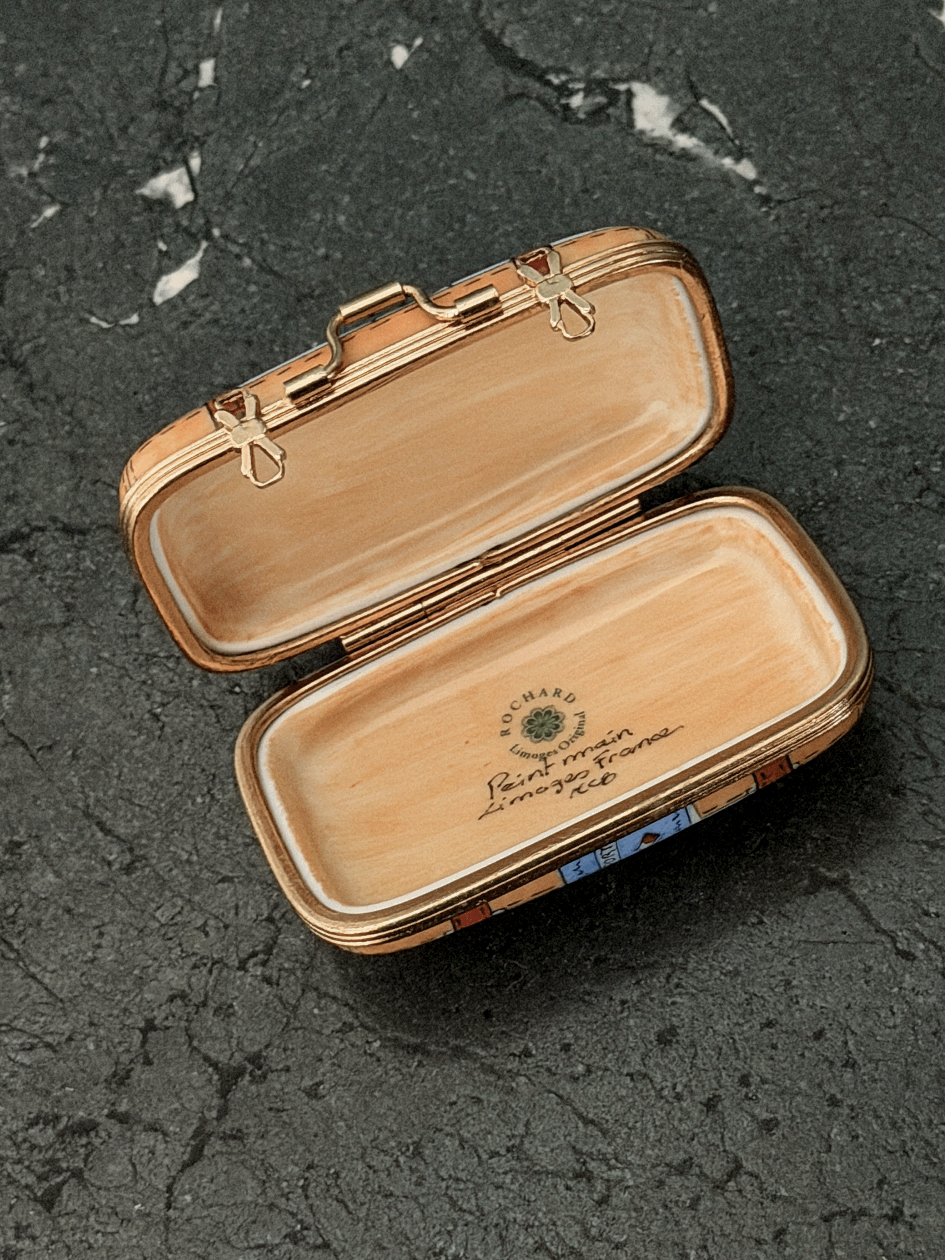 Opened interior of a Rochard map suitcase Limoges box showing a tan leather textile texture lining, the factory original workshop backstamp