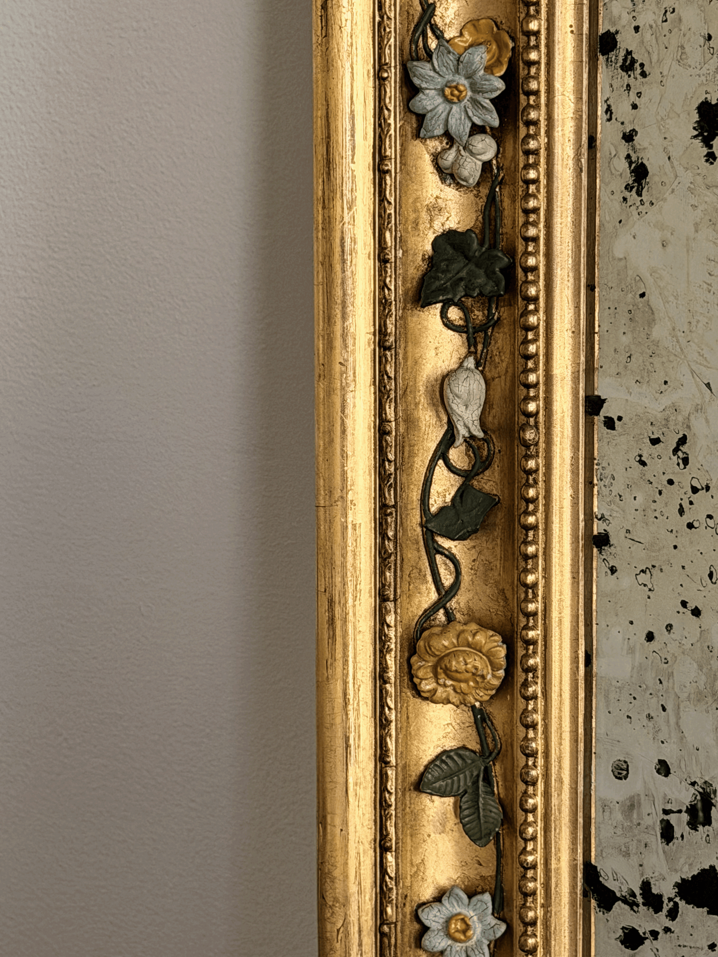 Close-up of a 19th-century French mirror frame showcasing hand-modeled porcelain white and yellow roses attached to hand-wrought dark metal vine moldings against a brilliant gold leaf gilded finish.