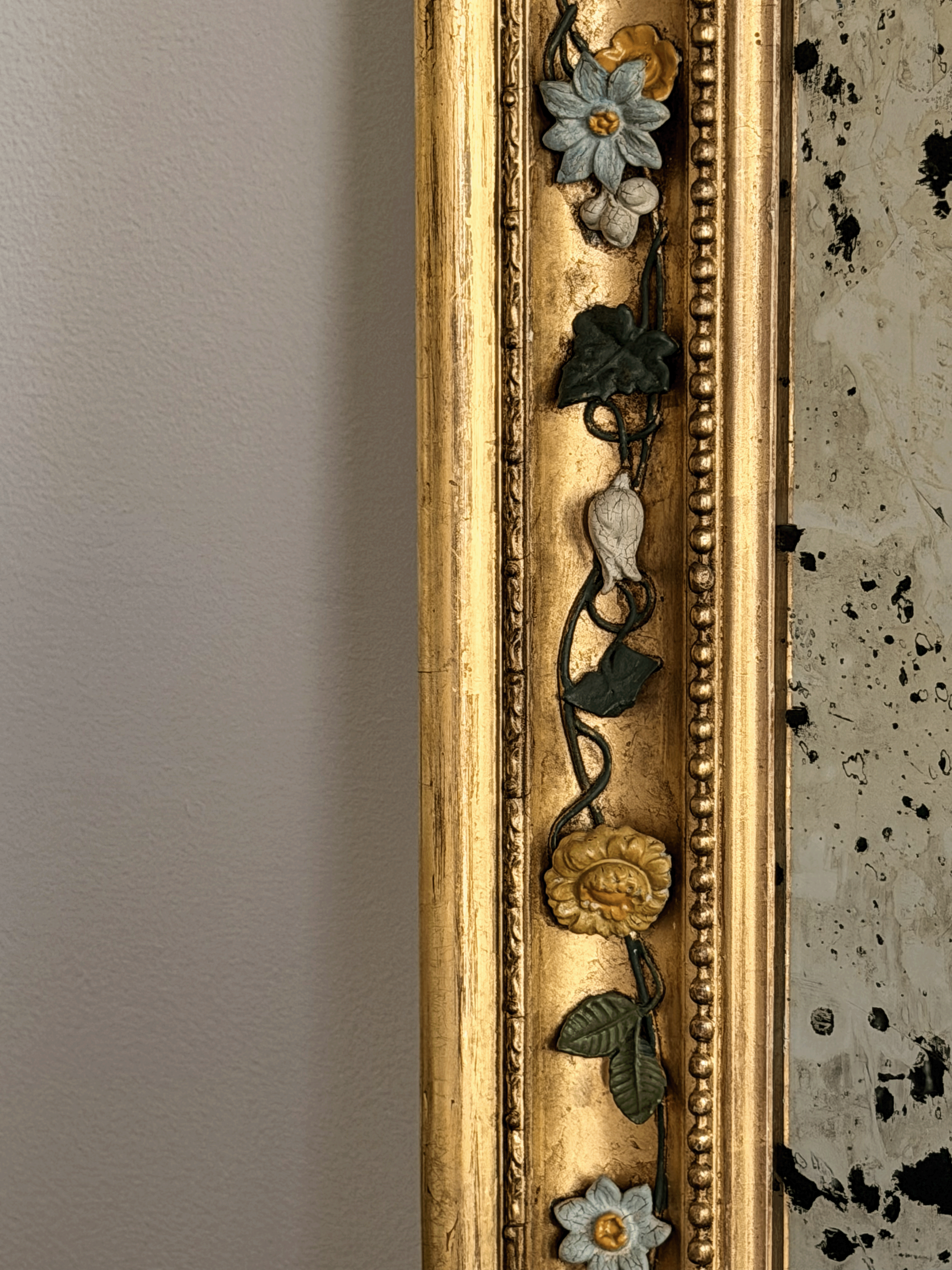Close-up of a 19th-century French mirror frame showcasing hand-modeled porcelain white and yellow roses attached to hand-wrought dark metal vine moldings against a brilliant gold leaf gilded finish.