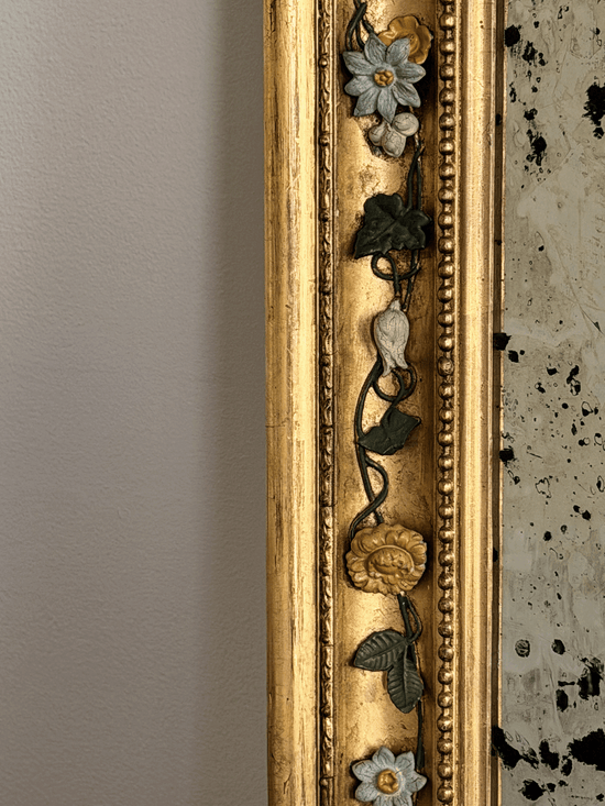 Close-up of a 19th-century French mirror frame showcasing hand-modeled porcelain white and yellow roses attached to hand-wrought dark metal vine moldings against a brilliant gold leaf gilded finish.