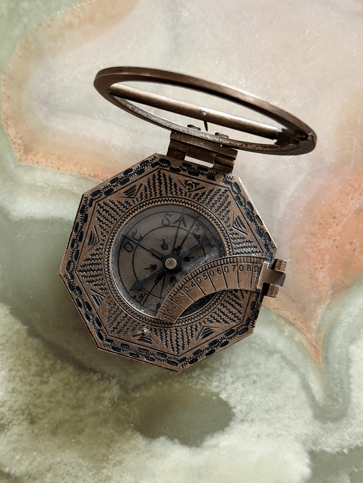 Vintage reproduction octagonal brass pocket equatorial sundial compass, featuring an antiqued dark-bronze finish with hand-stamped zig-zag geometric borders, a hinged sundial ring, and a folding side latitude arc.