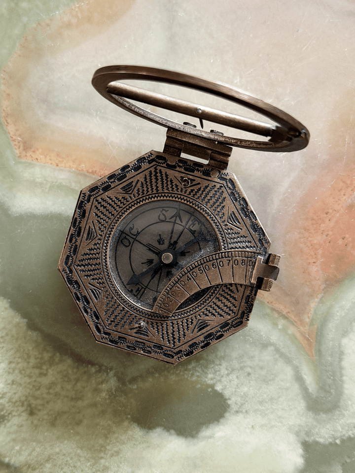 Vintage reproduction octagonal brass pocket equatorial sundial compass, featuring an antiqued dark-bronze finish with hand-stamped zig-zag geometric borders, a hinged sundial ring, and a folding side latitude arc.