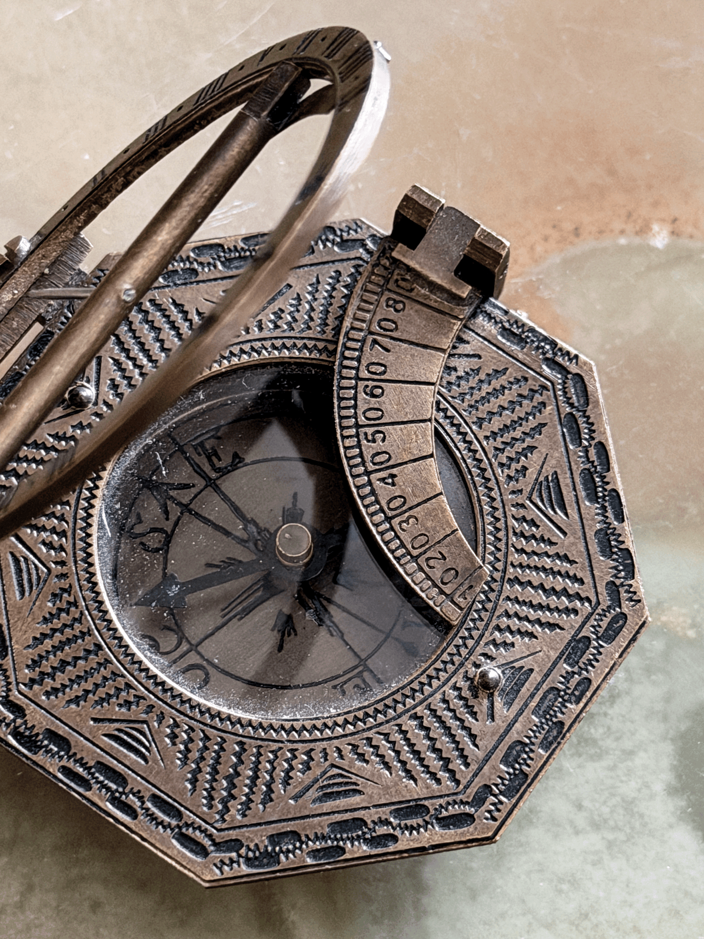 An antique-style octagonal brass or bronze pocket sundial with a hinged cover and rotating arm, close-up