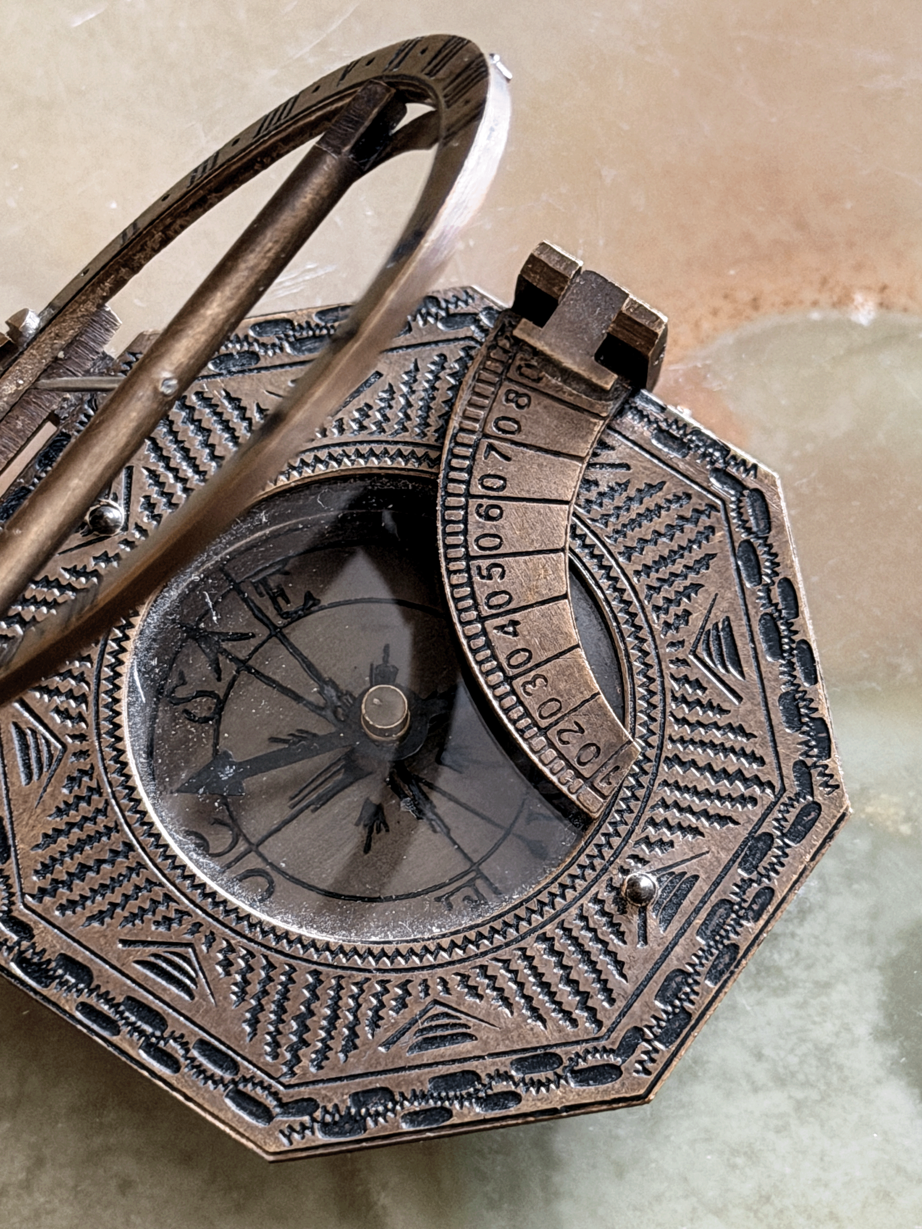 An antique-style octagonal brass or bronze pocket sundial with a hinged cover and rotating arm, close-up