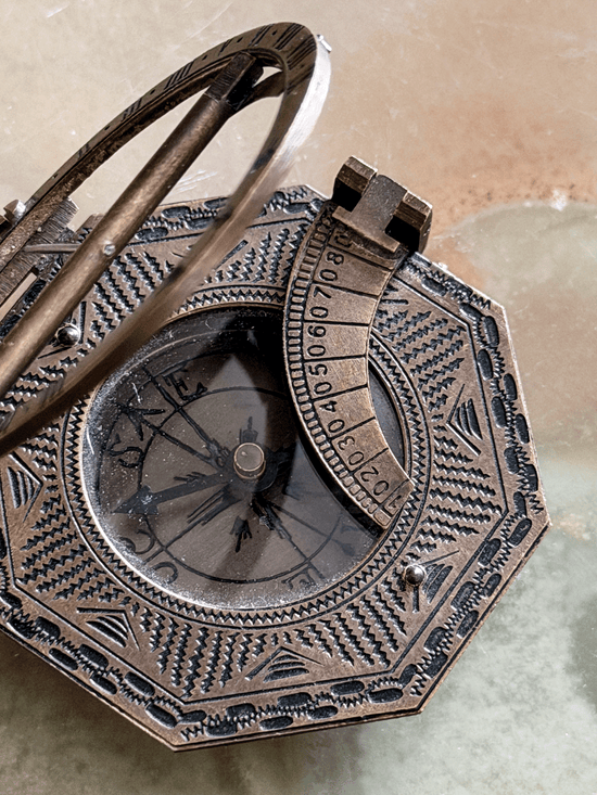 An antique-style octagonal brass or bronze pocket sundial with a hinged cover and rotating arm, close-up