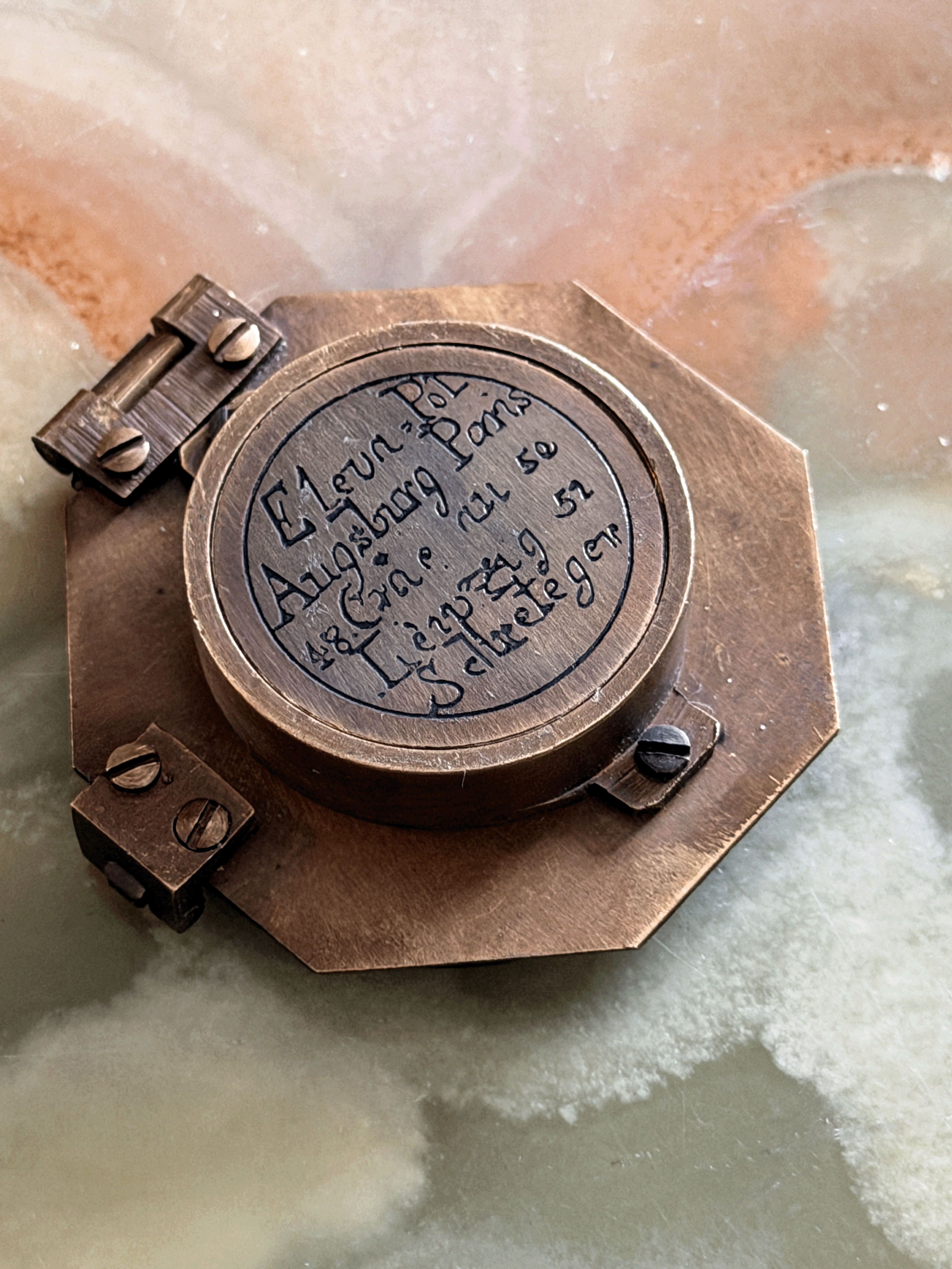 Engraved underside of a reproduction brass pocket sundial, replicating an 18th-century German instrument with an Elev. Pol. latitude table for Augsburg, Paris, Cracau, and Liège alongside the maker signature Schretegger.