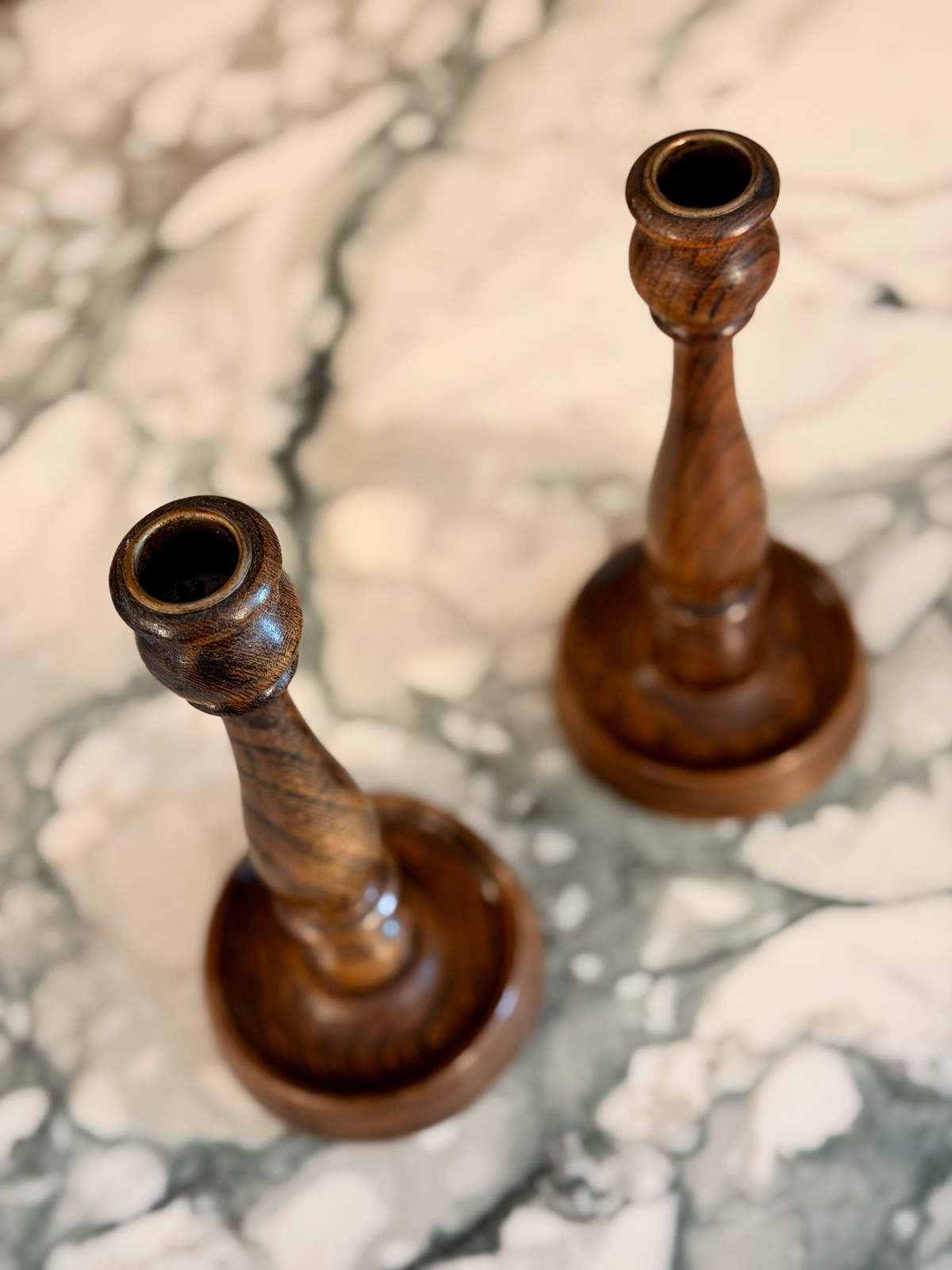 Two wooden candle holders on a marble surface; top down view