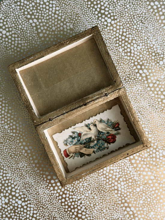 An open vintage-style wooden keepsake box with a gold-toned frame, showcasing a floral and bird illustration on the inner lining, set against a patterned beige and white background.