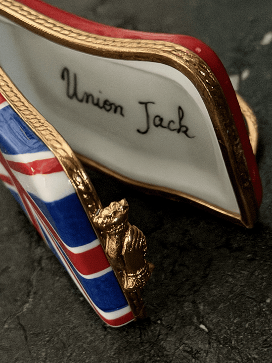 Hand-painted French porcelain Limoges box shaped like a wavy vintage kiss lock coin purse decorated with the British Union Jack flag, featuring an ornate brass frame and a three-dimensional miniature Royal Guard metal clasp latch.