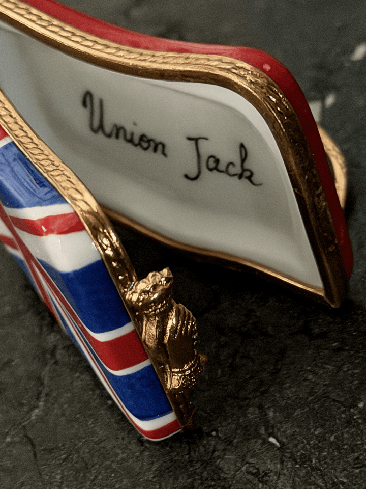Hand-painted French porcelain Limoges box shaped like a wavy vintage kiss lock coin purse decorated with the British Union Jack flag, featuring an ornate brass frame and a three-dimensional miniature Royal Guard metal clasp latch.