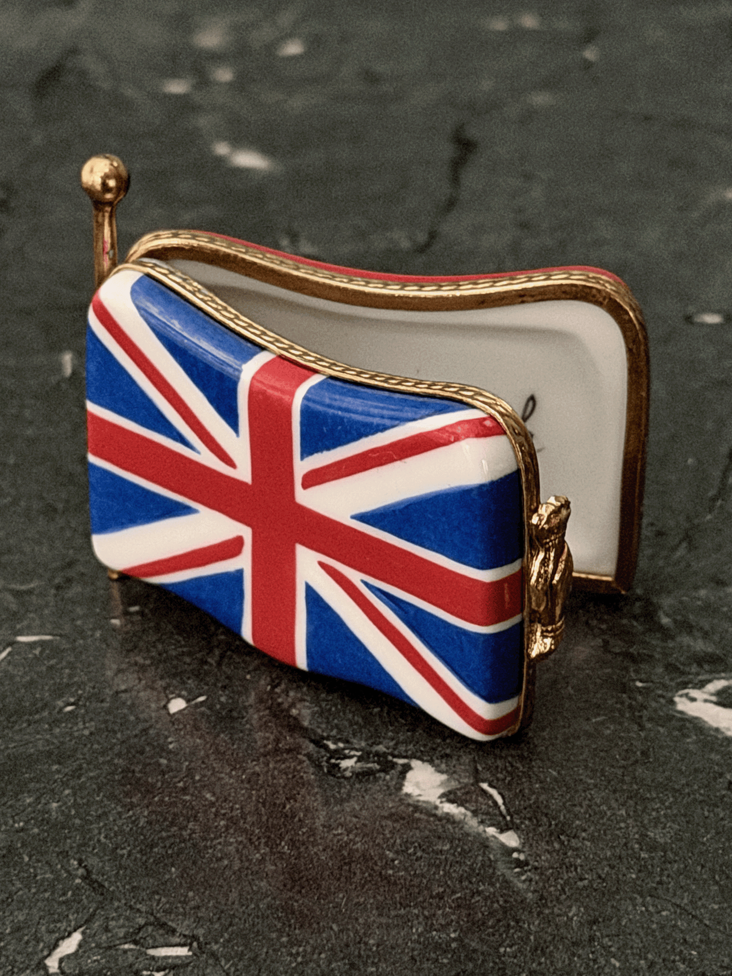 Hand-painted French porcelain Limoges box shaped like a wavy vintage kiss lock coin purse decorated with the British Union Jack flag, featuring an ornate brass frame and a three-dimensional miniature Royal Guard metal clasp latch.