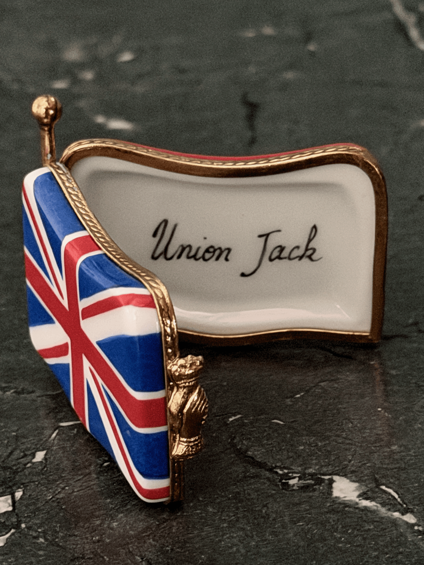 Hand-painted French porcelain Limoges box shaped like a wavy vintage kiss lock coin purse decorated with the British Union Jack flag, featuring an ornate brass frame and a three-dimensional miniature Royal Guard metal clasp latch.