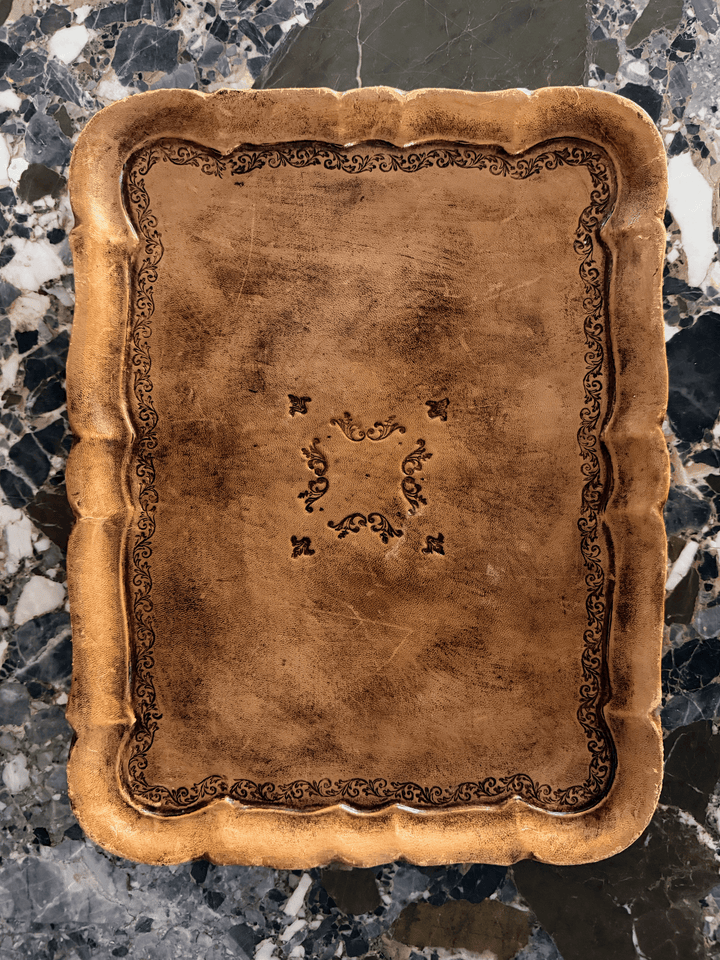 A square decorative tray with a scalloped rim and embossed floral border detailing, shown from a top-down view on a dark marble surface.