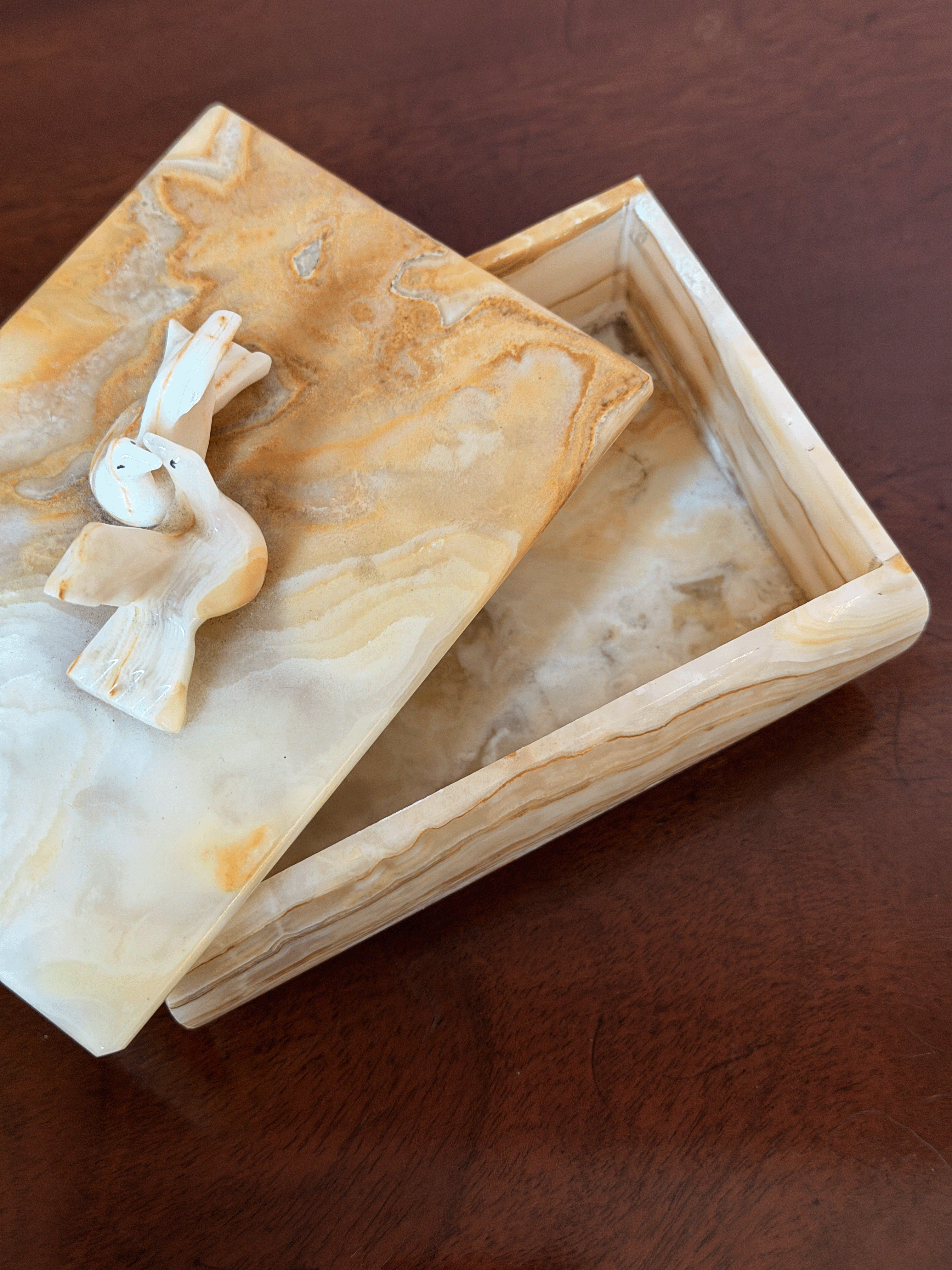 A rectangular marble keepsake box with a matching lid, featuring carved doves on top, set on a dark brown wooden surface.