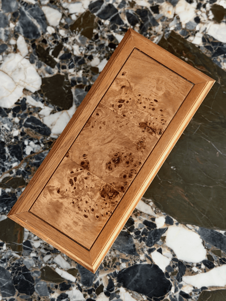 A rectangular wooden box with a rich burl wood grain pattern and a polished beveled frame, shown diagonally on a marble surface.