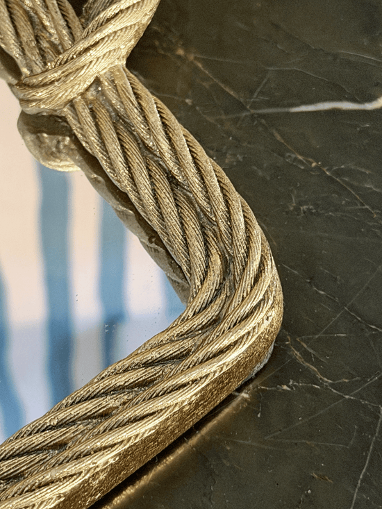 A close-up of a thick, twisted metallic cable with a gold finish, wrapped around a mirrored tray
