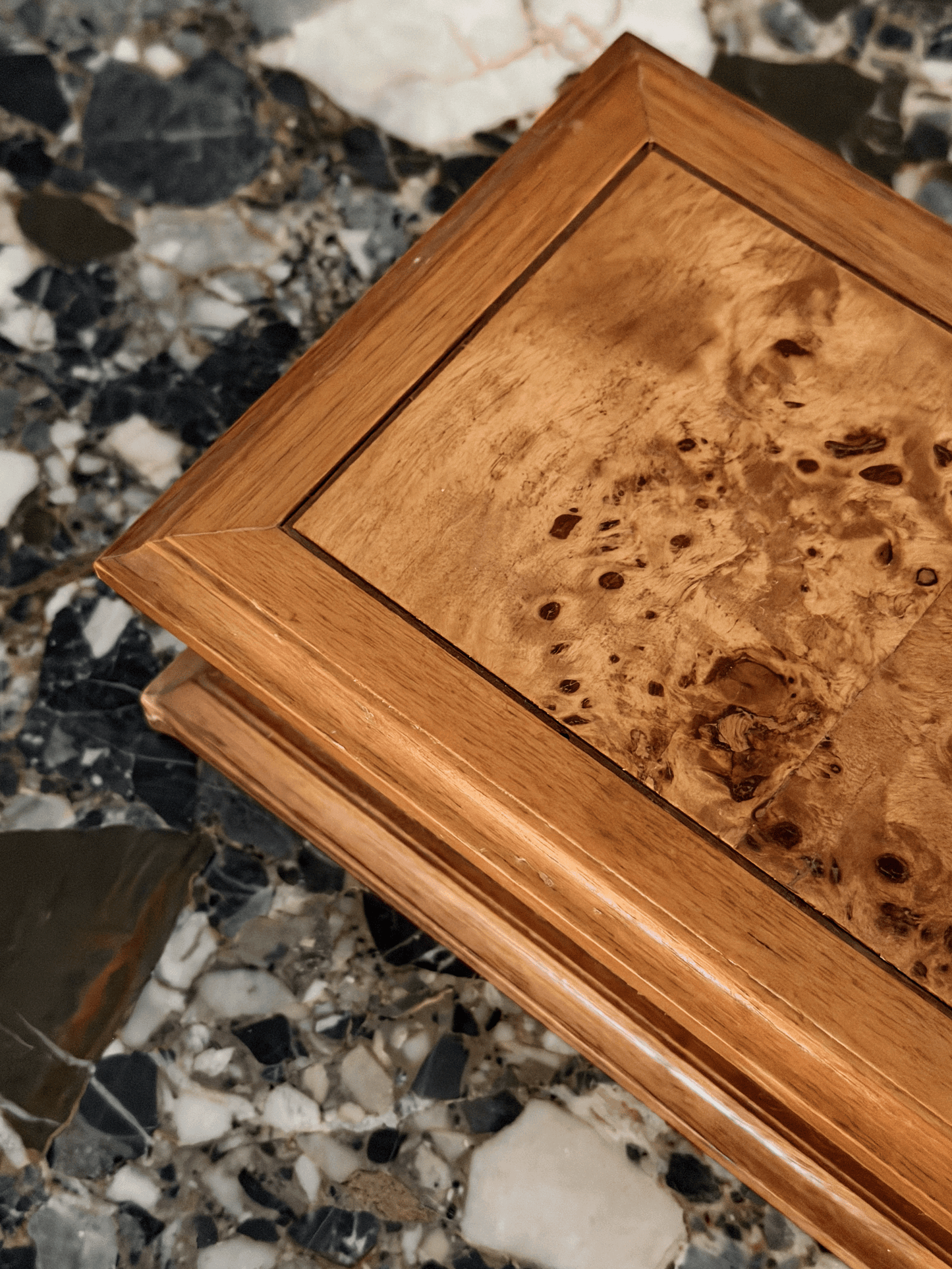 A close-up of a burl wooden box and beveled edges, set against a dark marble surface