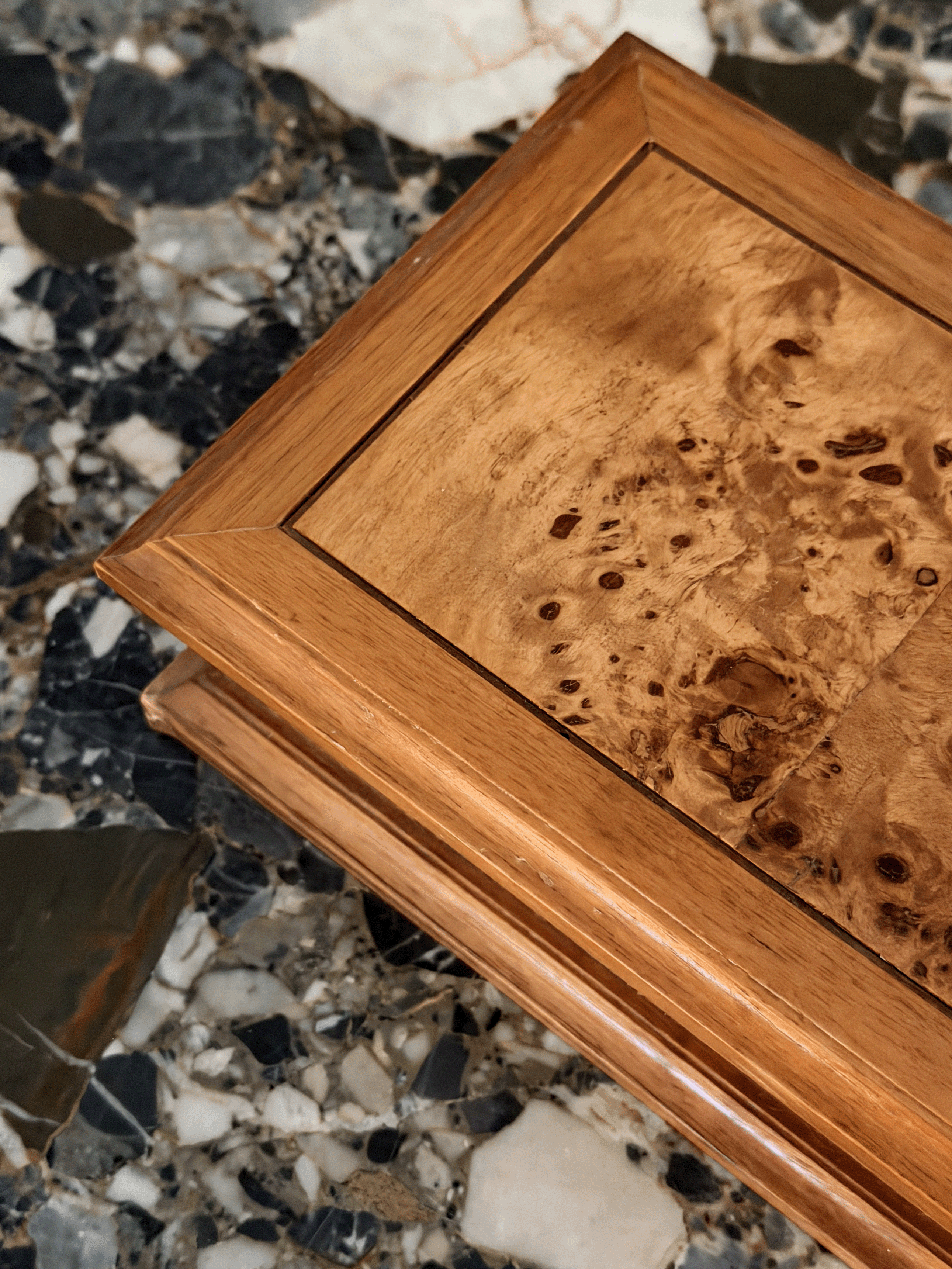 A close-up of a burl wooden box and beveled edges, set against a dark marble surface